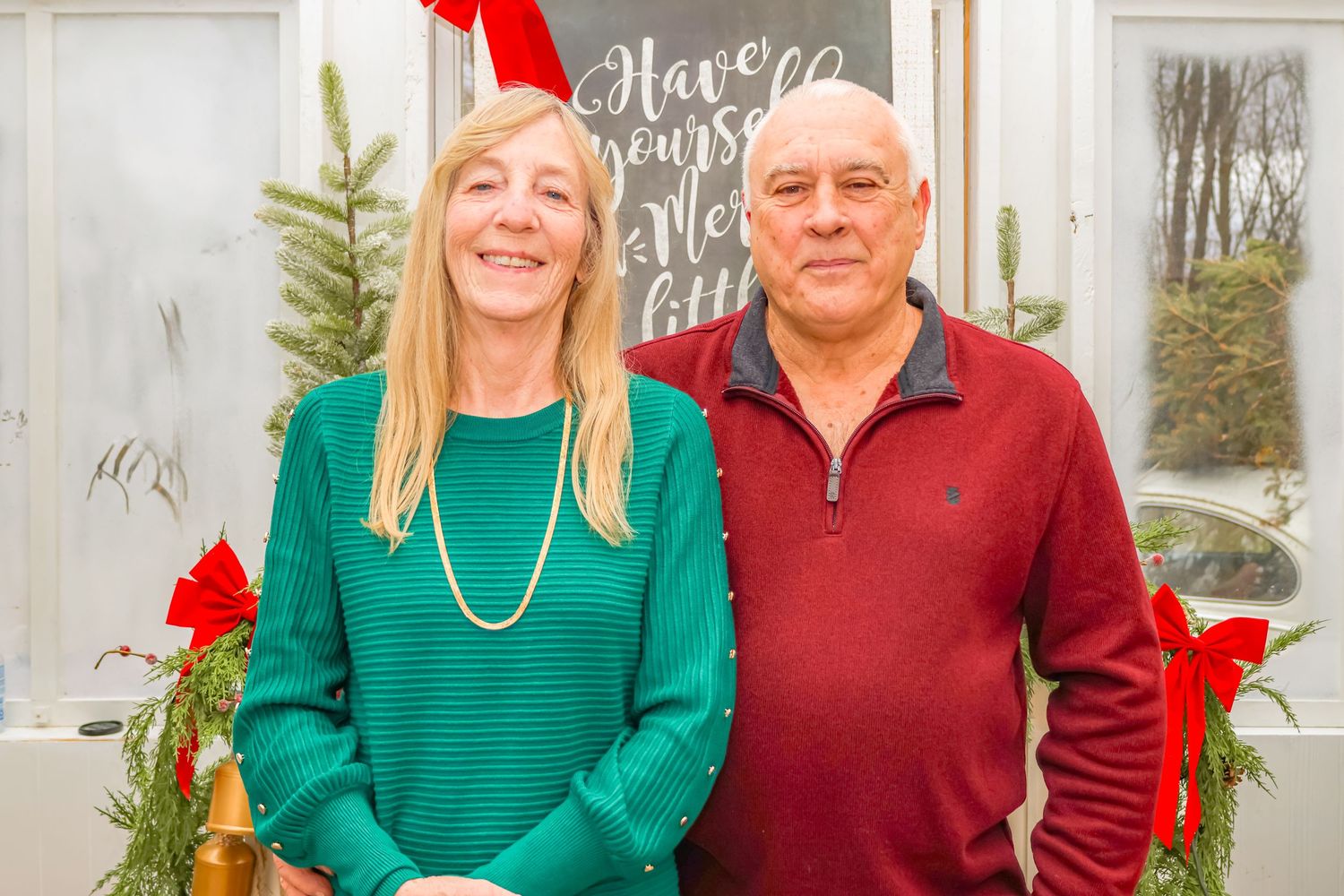 Two people in festive sweaters share a joyful moment in front of holiday decorations.