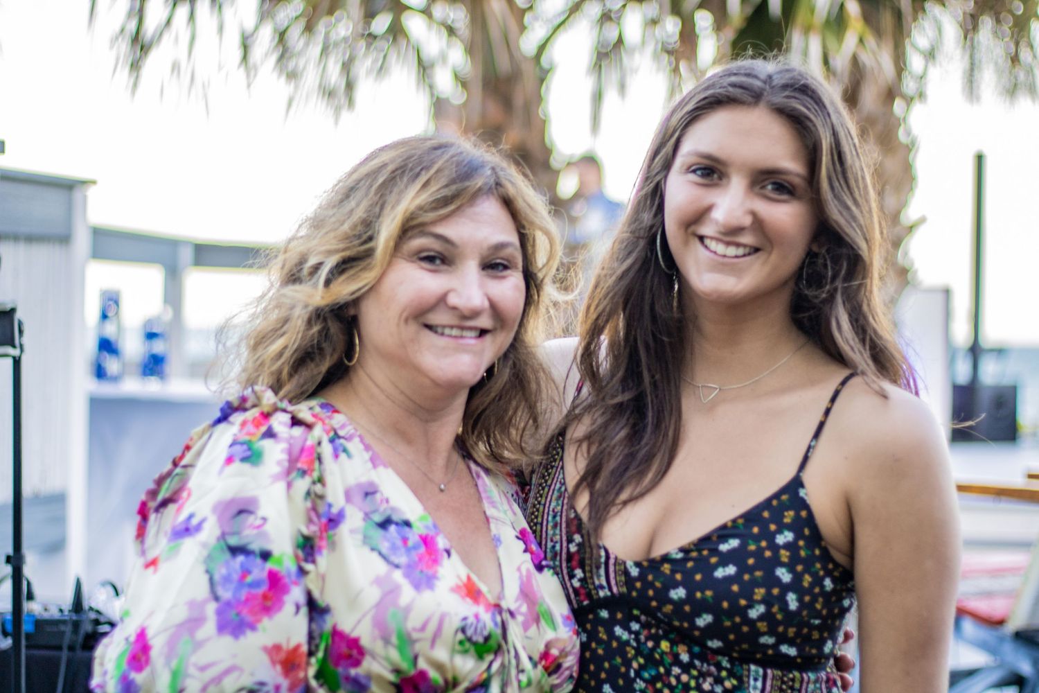Two guests share a moment at an outdoor celebration with palm trees visible.