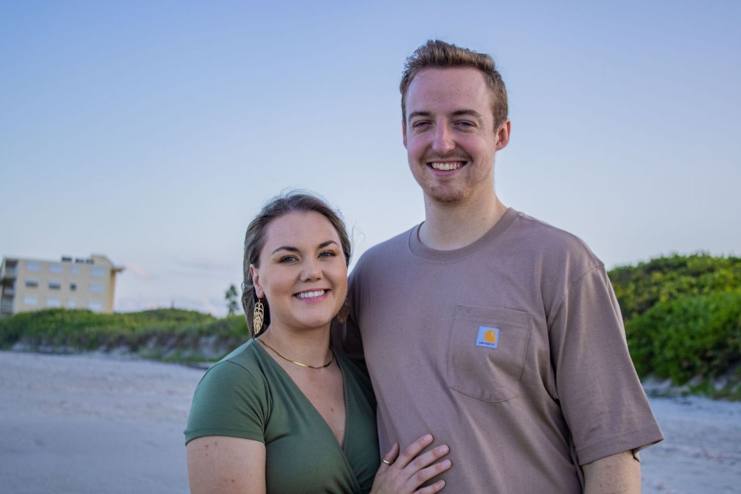 Couple smiling together on beach at sunset wearing casual clothing.