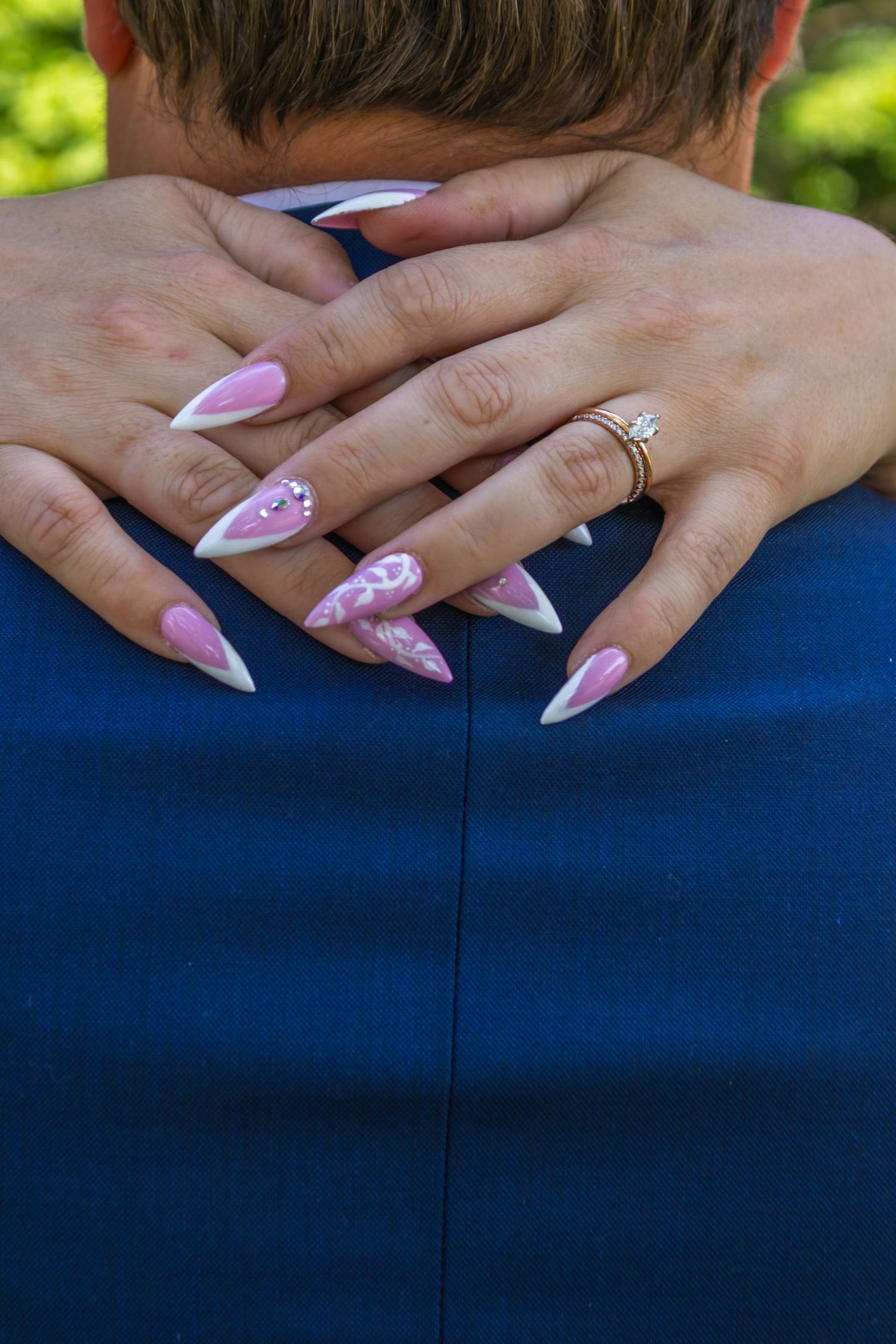 Close-up of hands with pink and white decorated stiletto nails and engagement ring against a navy blue background.