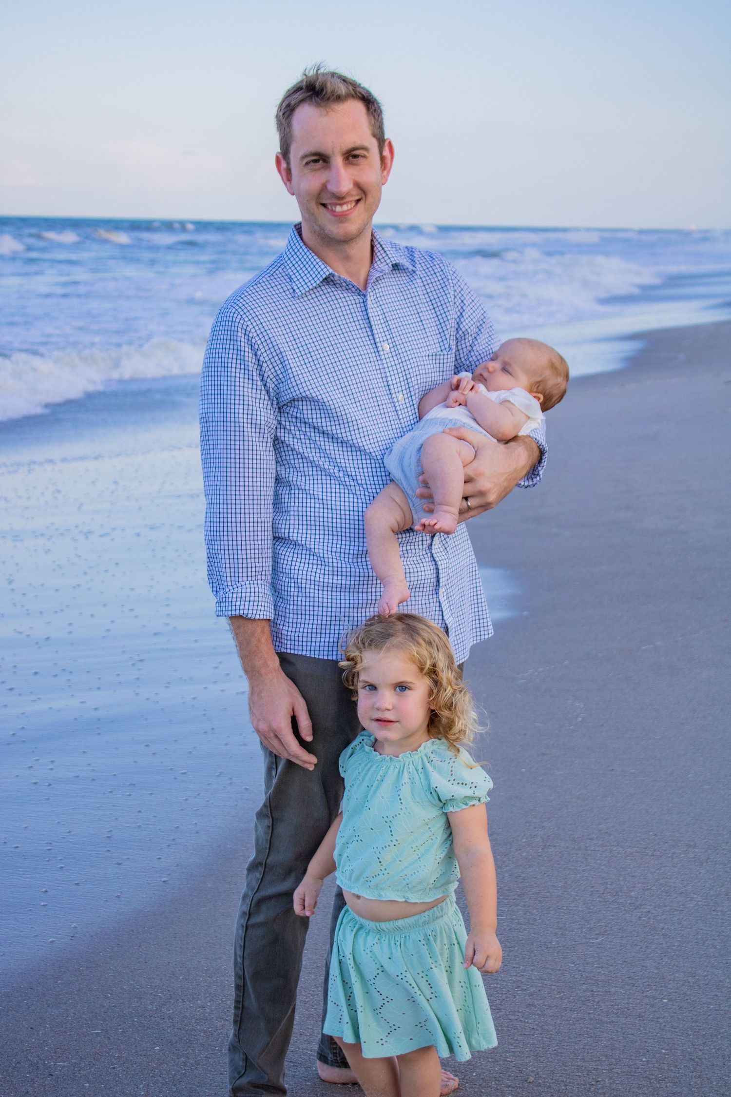 A family enjoying a sunset moment together on a beach with waves in the background.