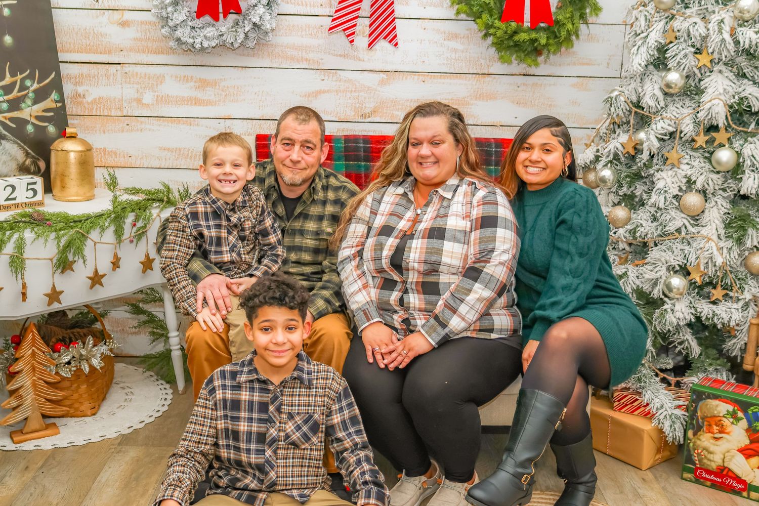 Family sitting together in front of a Christmas backdrop with decorative wreaths and a decorated tree.