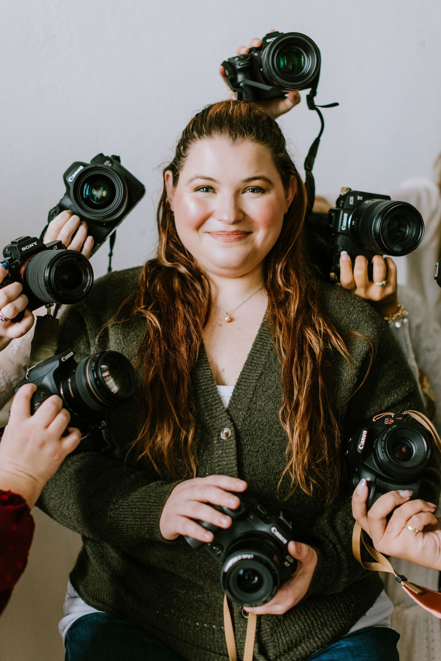 Photographer surrounded by multiple DSLR cameras while wearing a green cardigan.