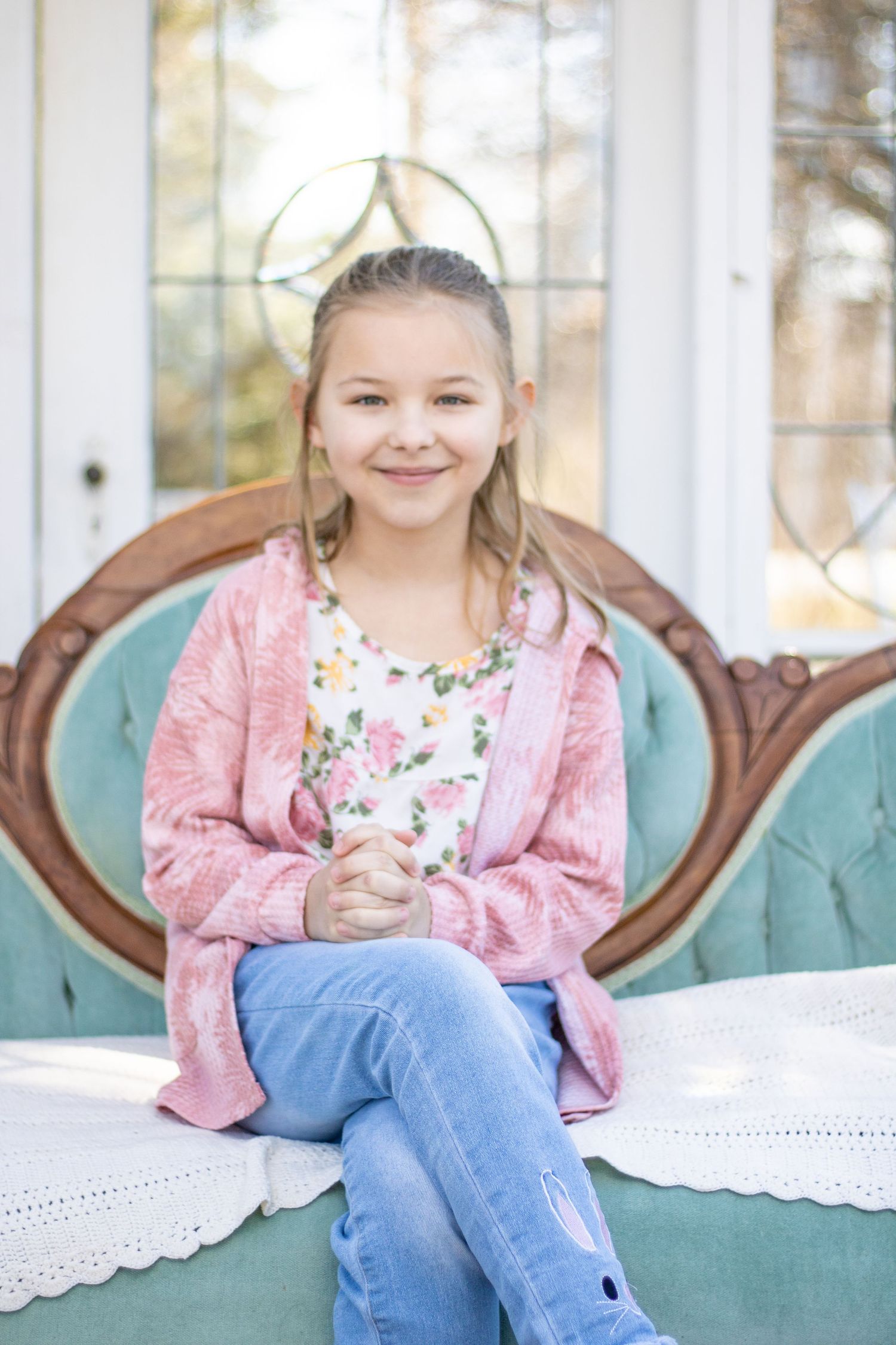 A child in pink sweater and jeans sitting on a turquoise vintage couch.