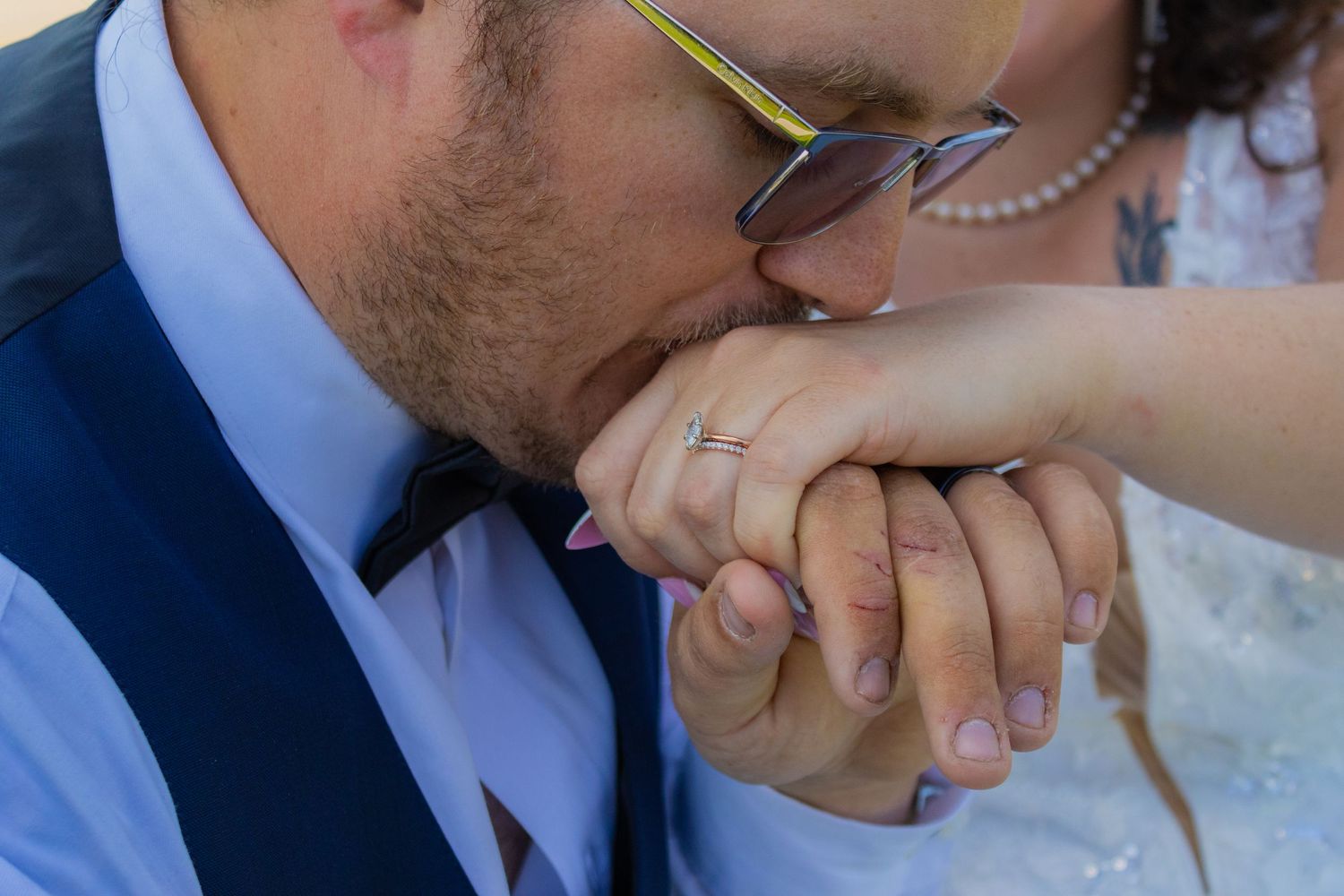 Close-up shot of groom kissing bride's hand, showing wedding ring details.