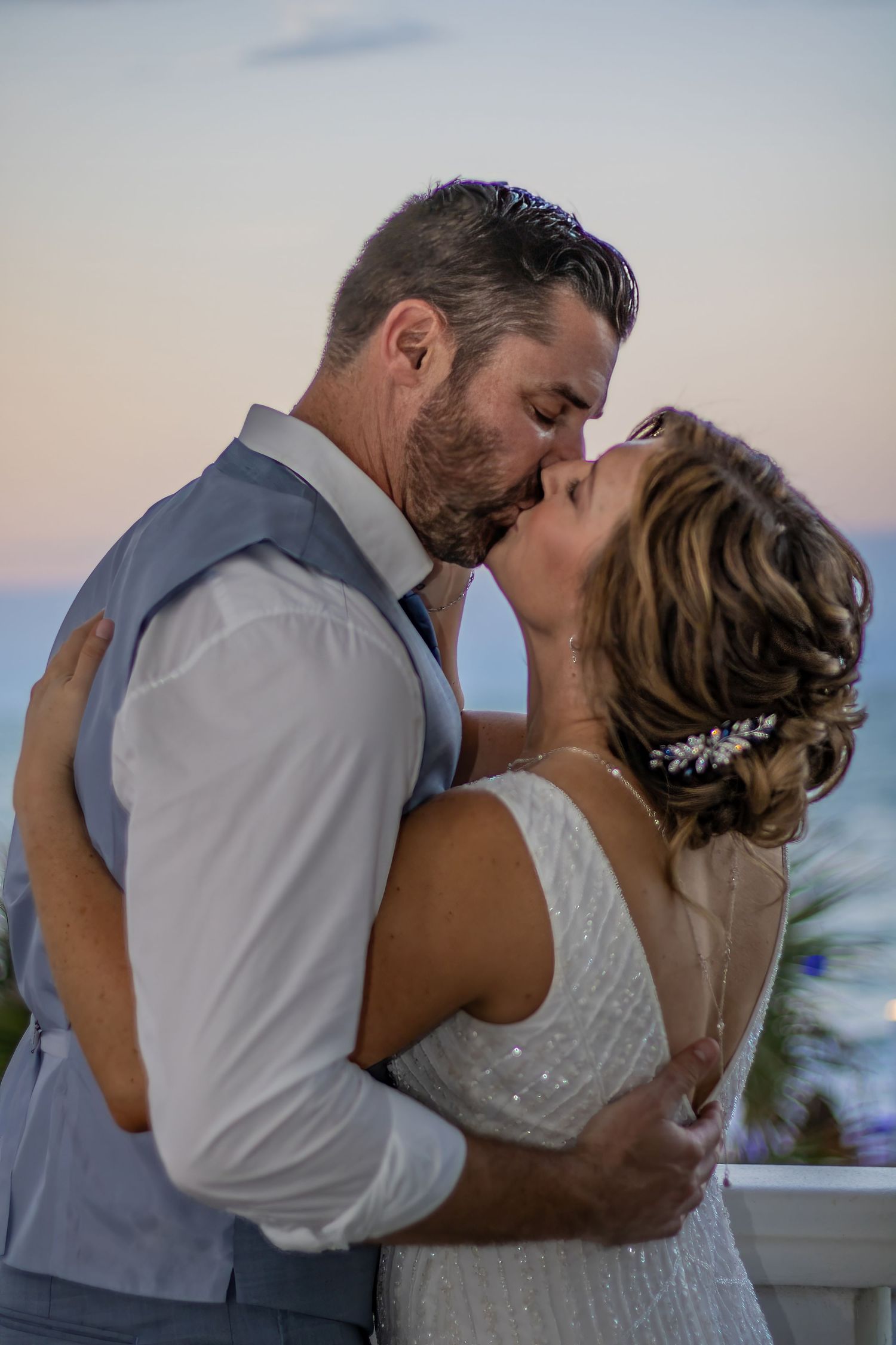 An intimate sunset moment between newlyweds sharing a passionate kiss on their wedding day.