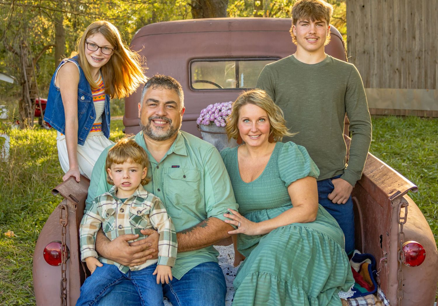 A family poses together in the bed of a vintage pickup truck on a sunny autumn afternoon.