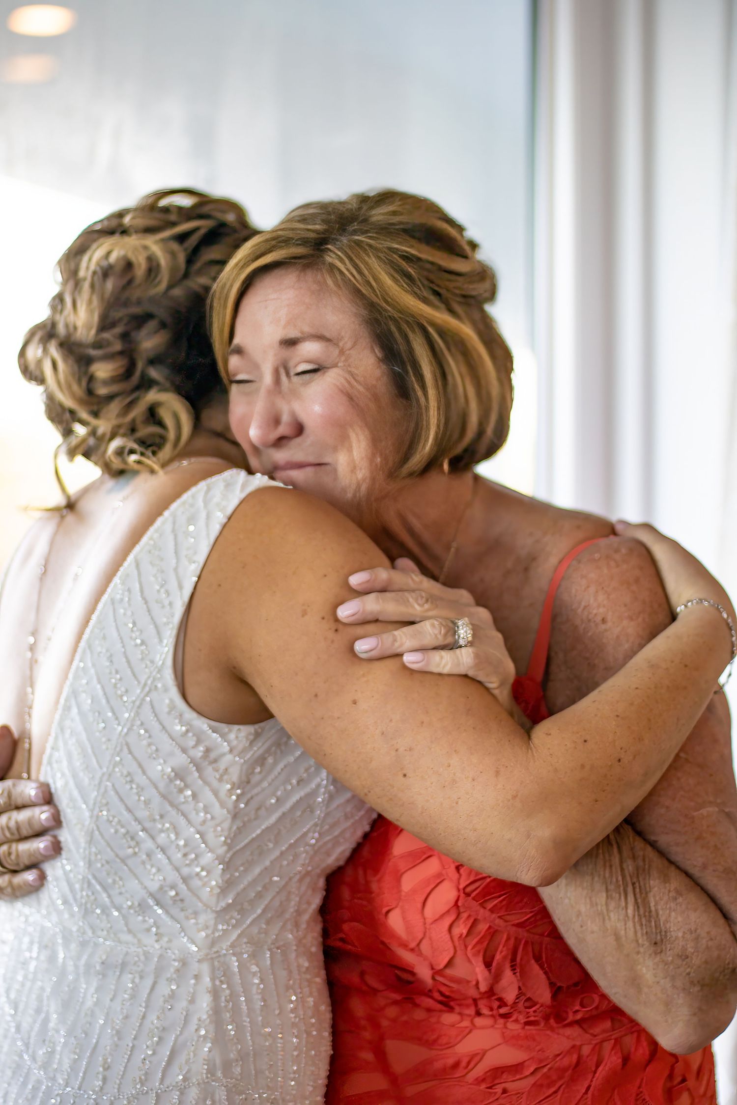 An emotional embrace shared during a wedding celebration in a sunlit room.