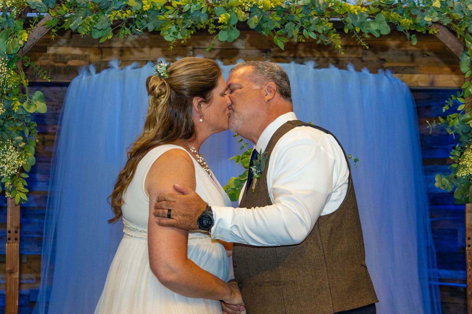Wedding kiss moment under blue fabric backdrop with greenery.