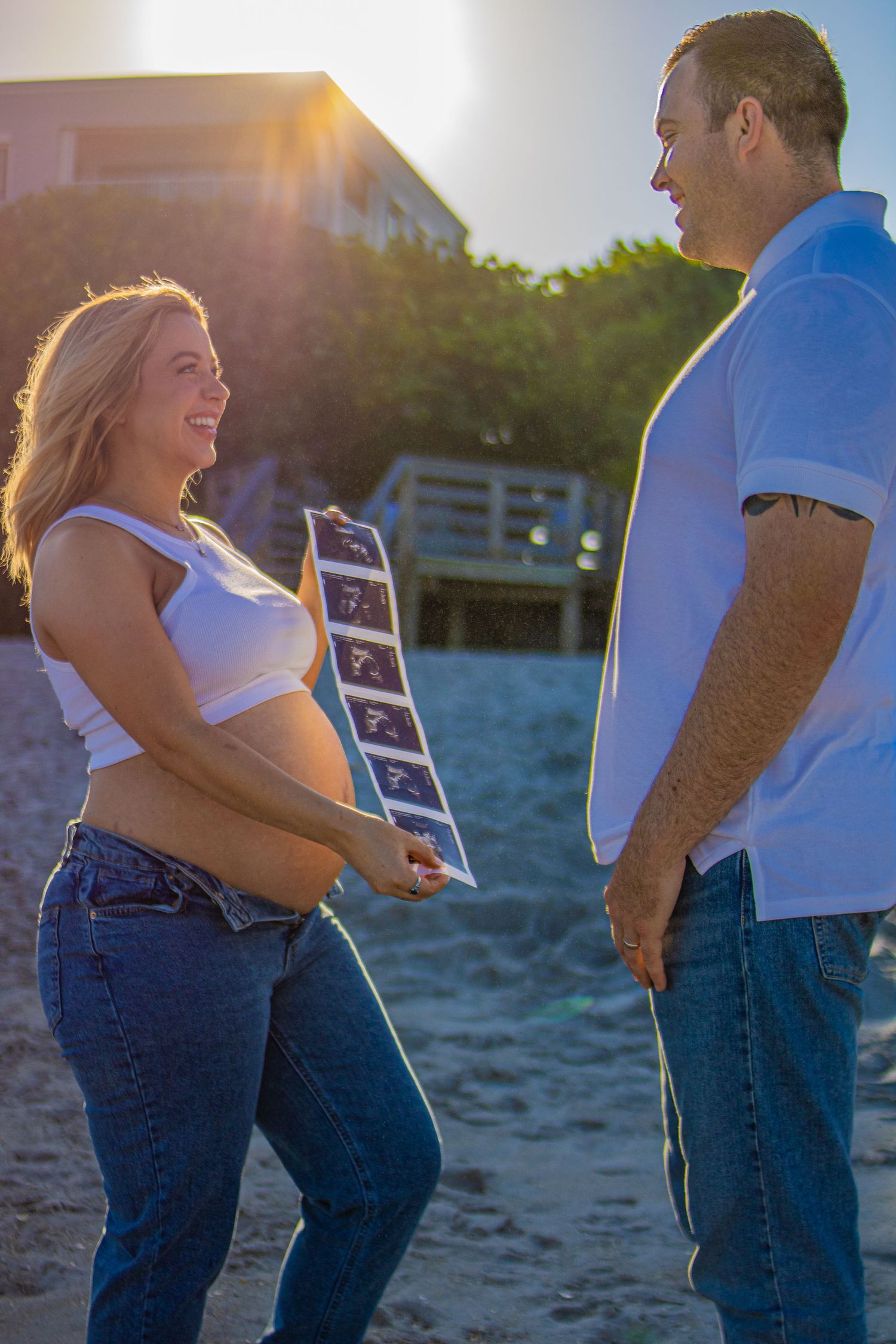 Couple on beach sharing ultrasound photos during sunset maternity photoshoot.
