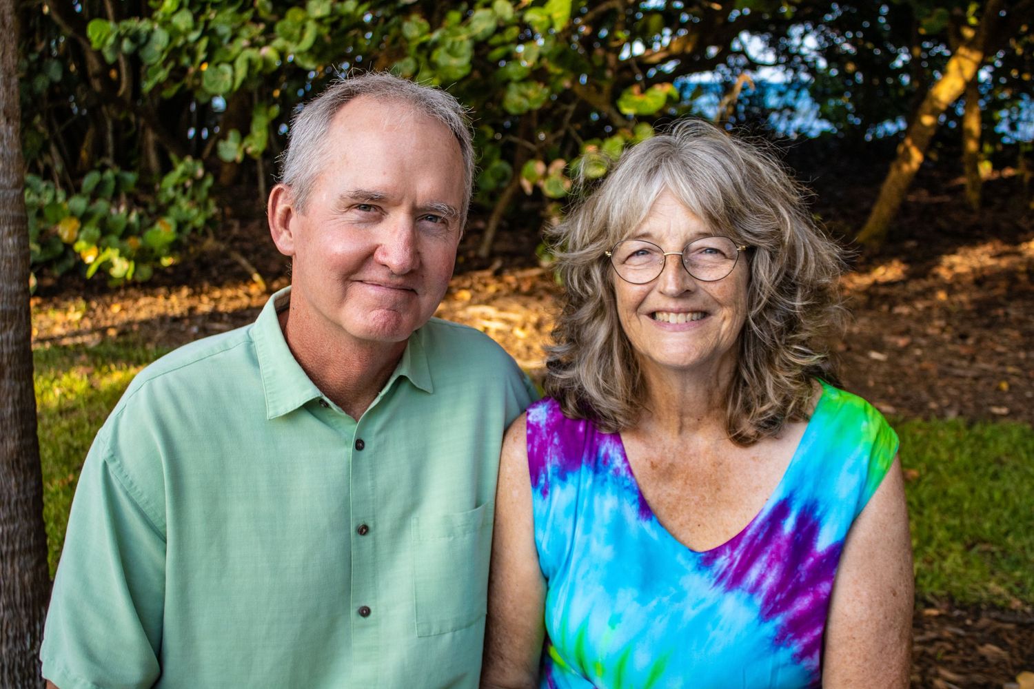 Senior couple in casual attire smiles for outdoor portrait.
