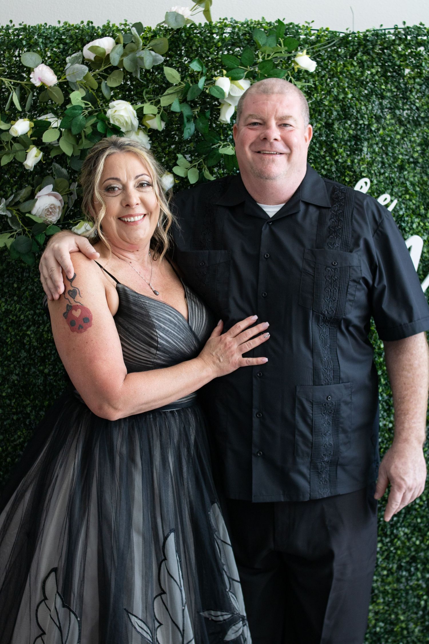 Couple poses against green floral wall backdrop at formal event with bride wearing elegant black tulle gown.