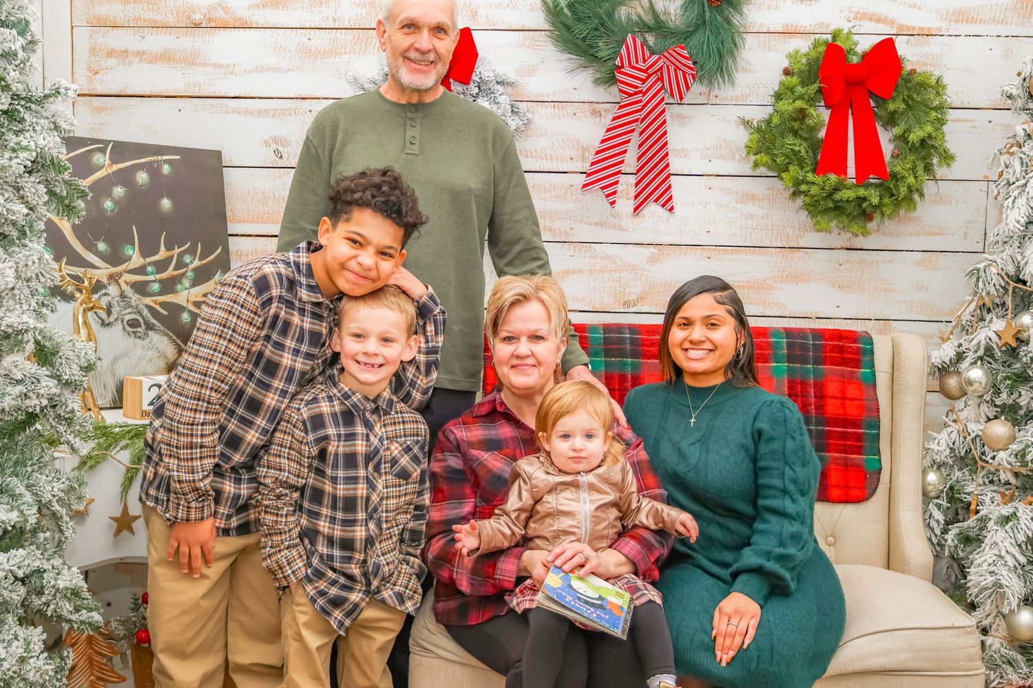 A family gathers for a holiday photo with Christmas wreaths and decorations in the background.