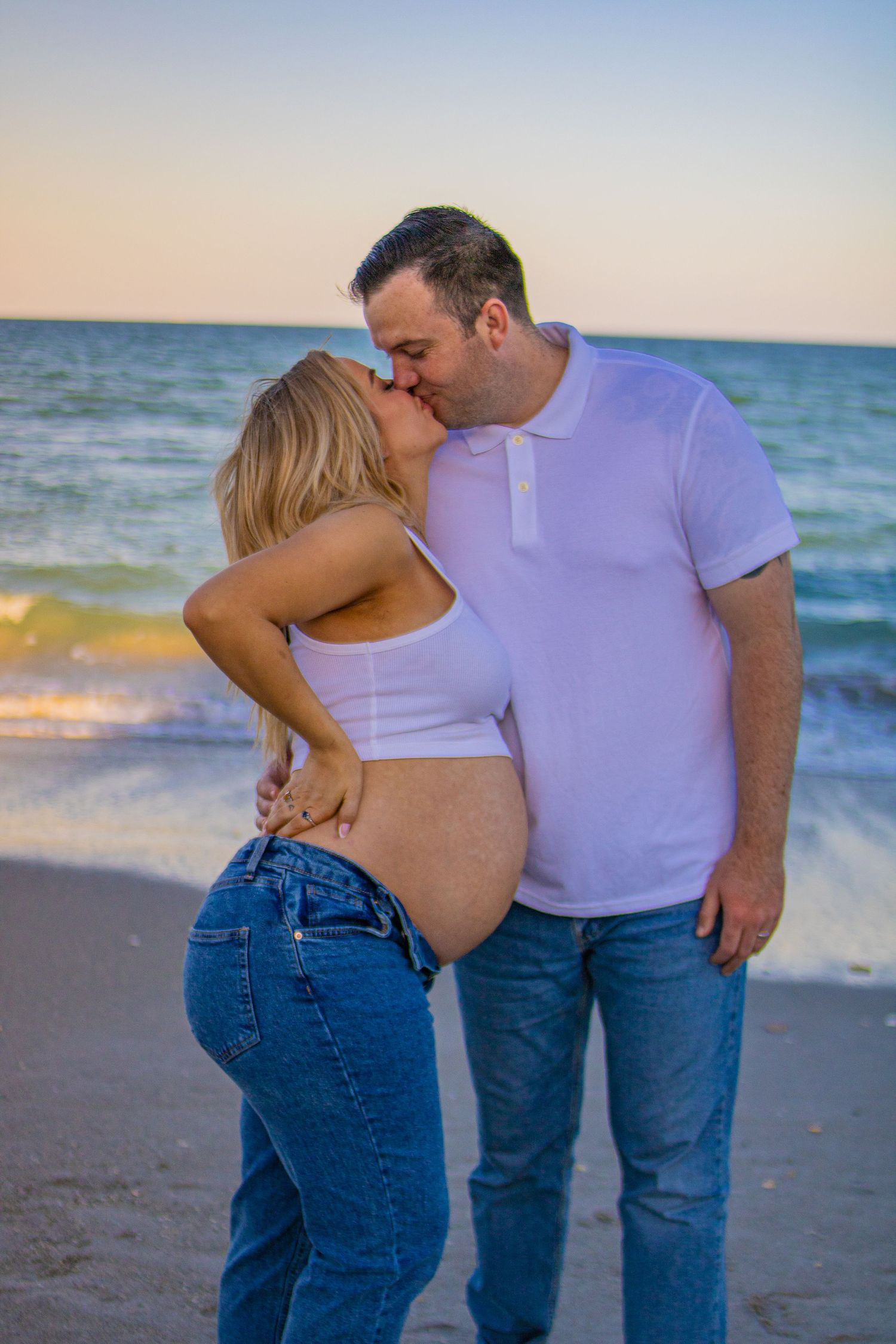 Romantic maternity photoshoot at beach with couple embracing during golden hour.