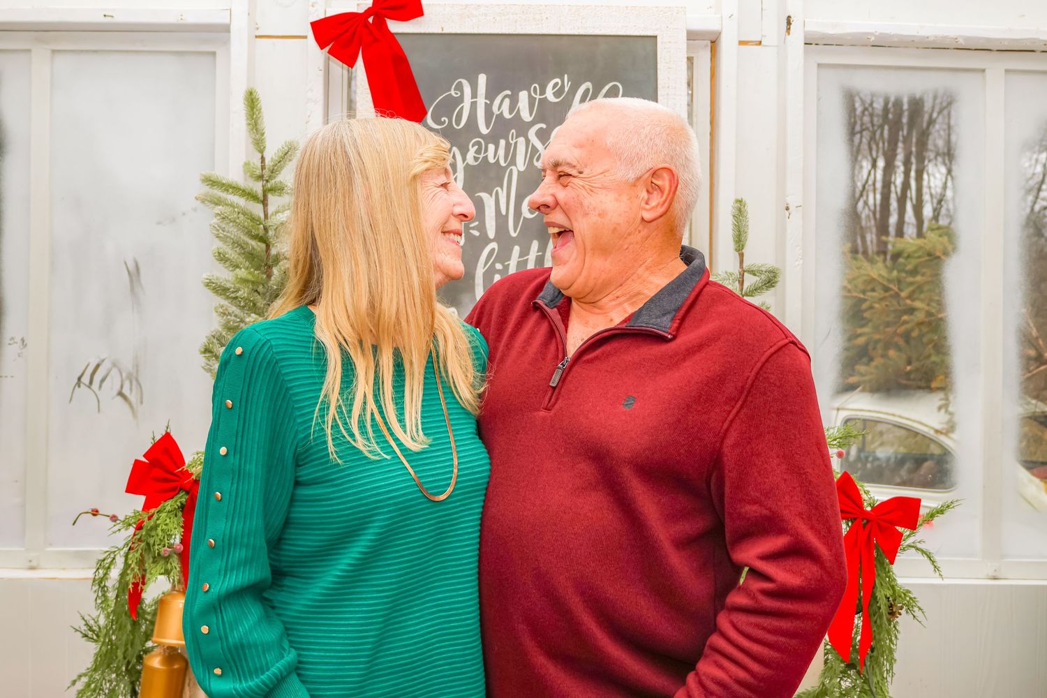 Two people in contrasting green and red sweaters share a laughing moment among holiday decorations.