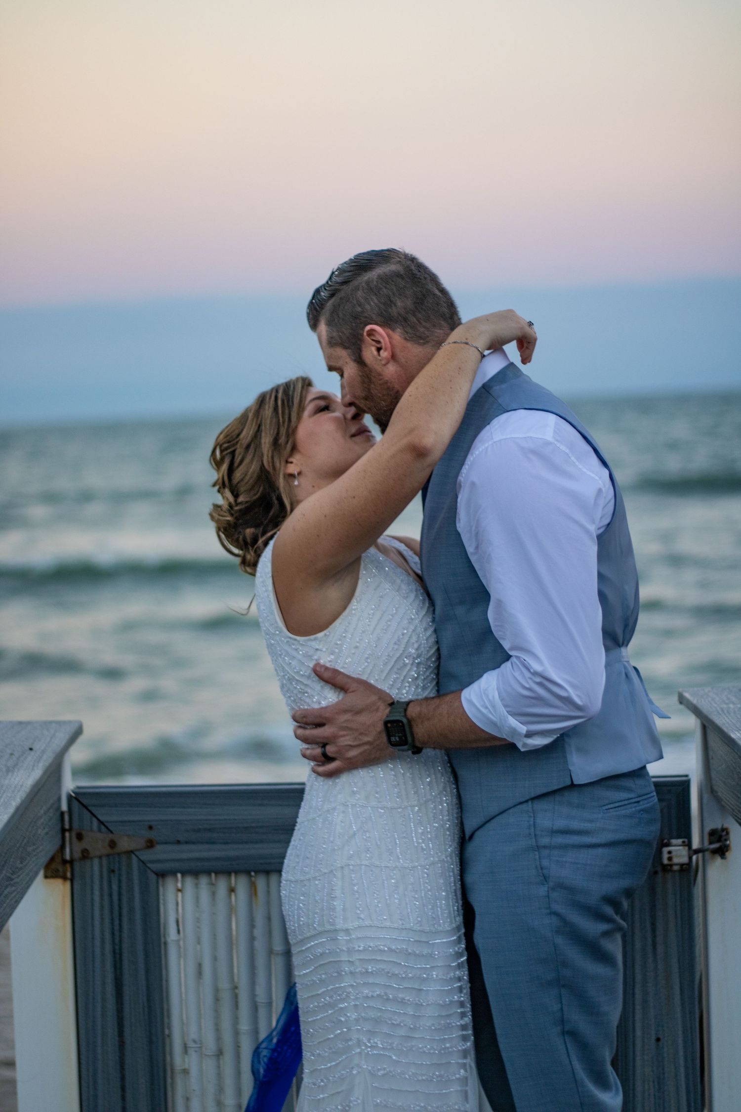 A romantic sunset embrace between newlyweds on a coastal boardwalk.