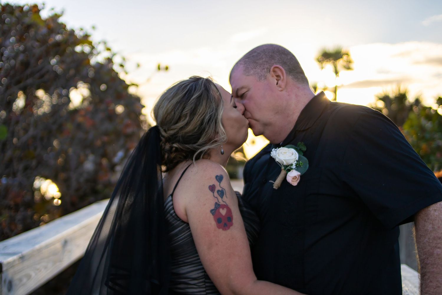 Silhouetted couple sharing romantic sunset kiss on boardwalk.