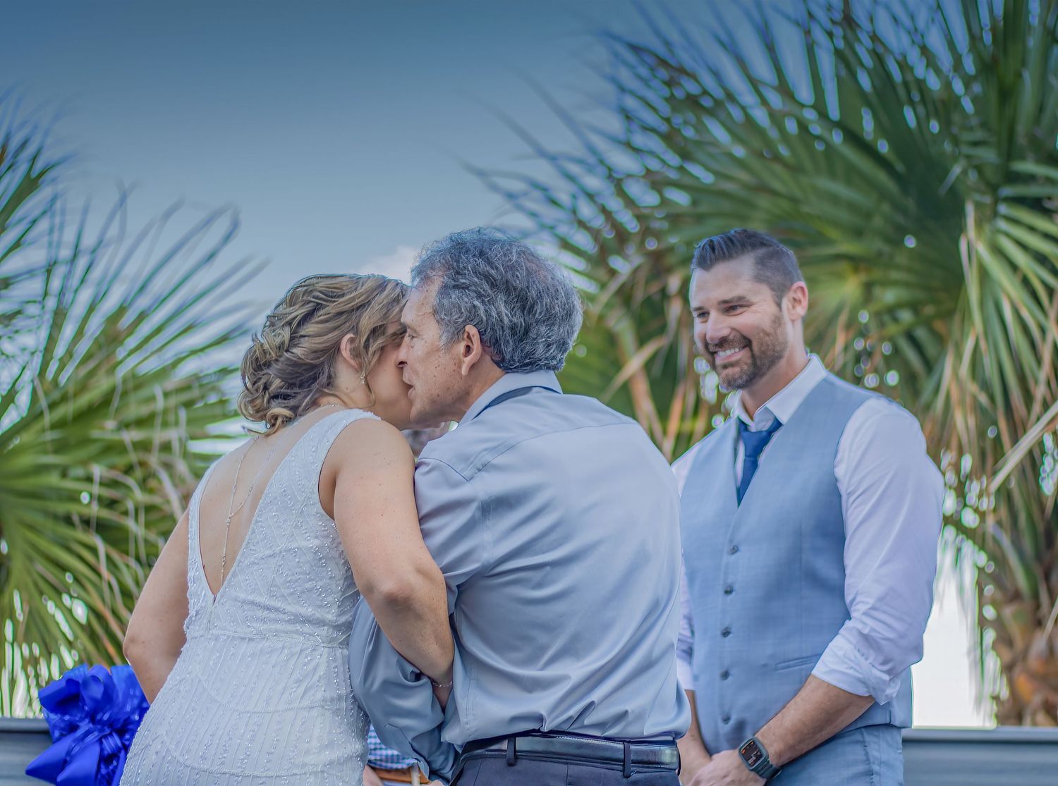 A wedding ceremony moment outdoors with palm trees in the background.