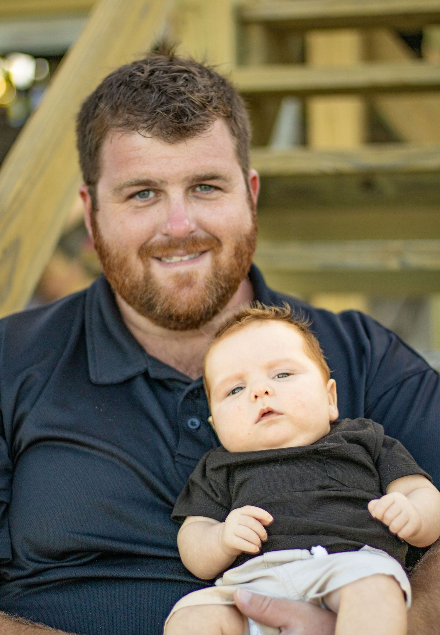 Parent and infant wearing black outfit pose together on wooden deck stairs.