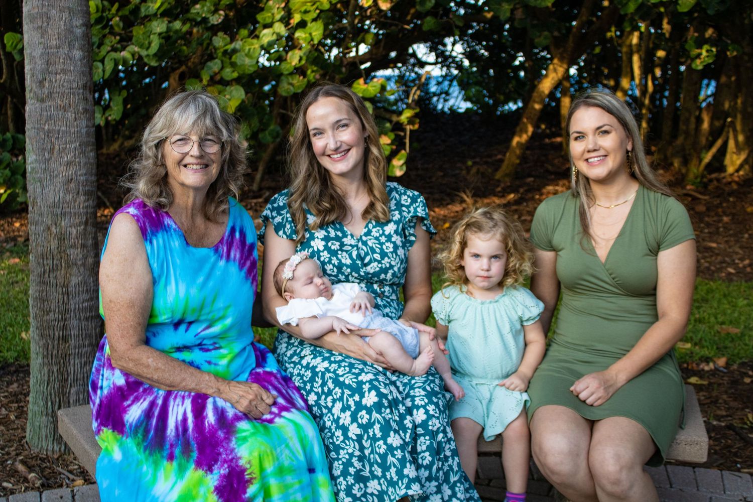 Three generations of women and children pose together in outdoor garden setting.