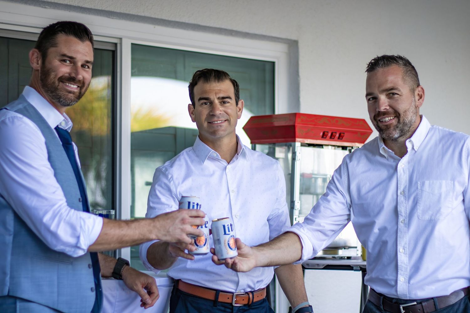 Three groomsmen in light blue suits share drinks during wedding festivities.