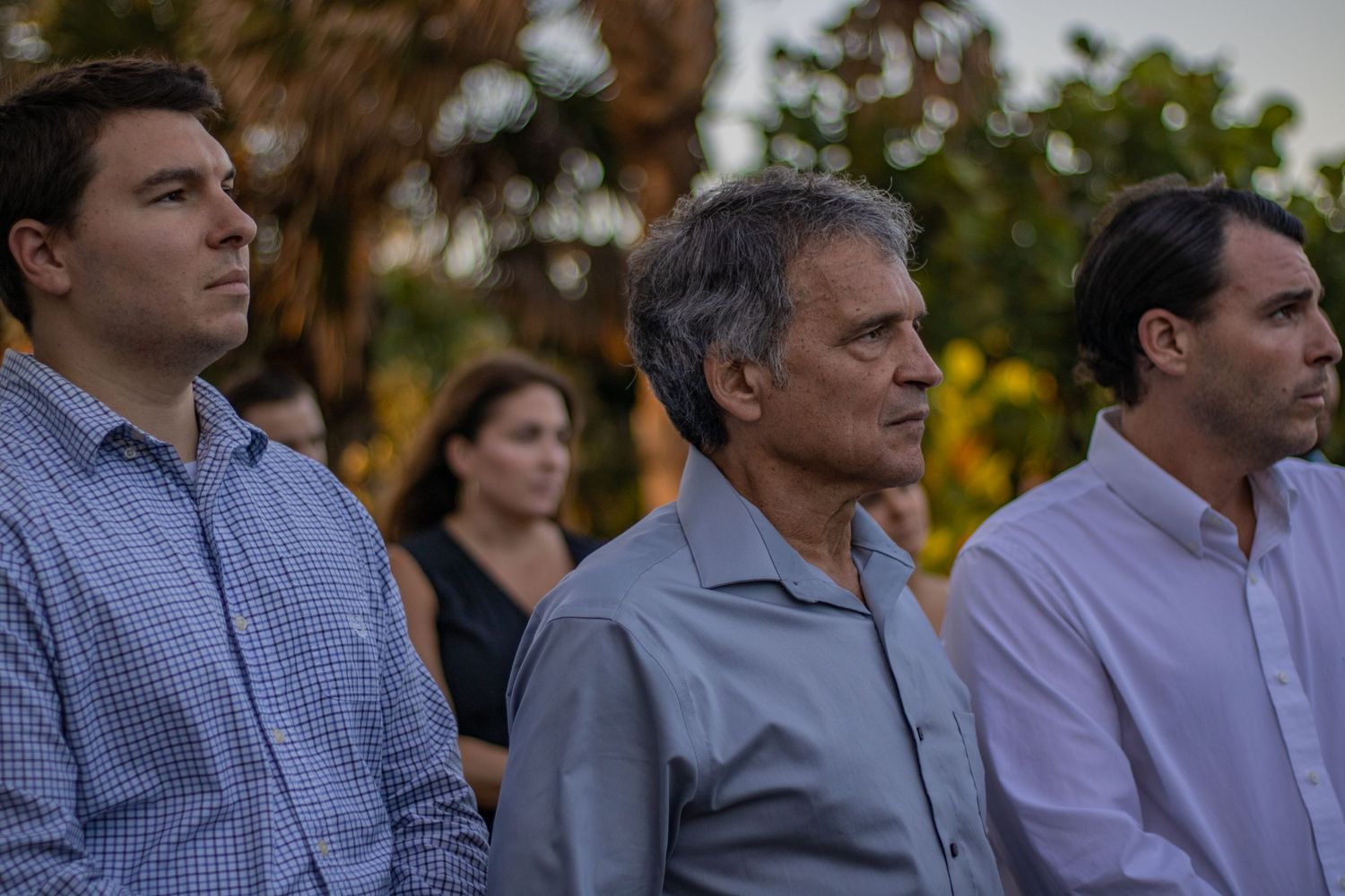 Three guests stand together at an outdoor gathering during sunset.