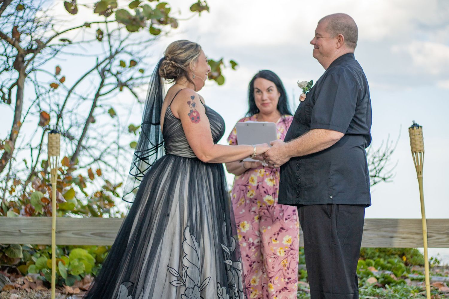 An outdoor wedding ceremony takes place with a couple exchanging vows before an officiant.