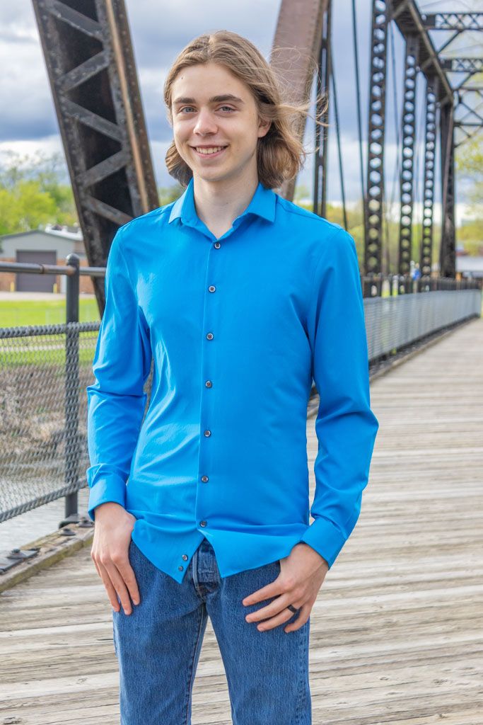 A person in a bright blue button-down shirt poses on a wooden bridge.