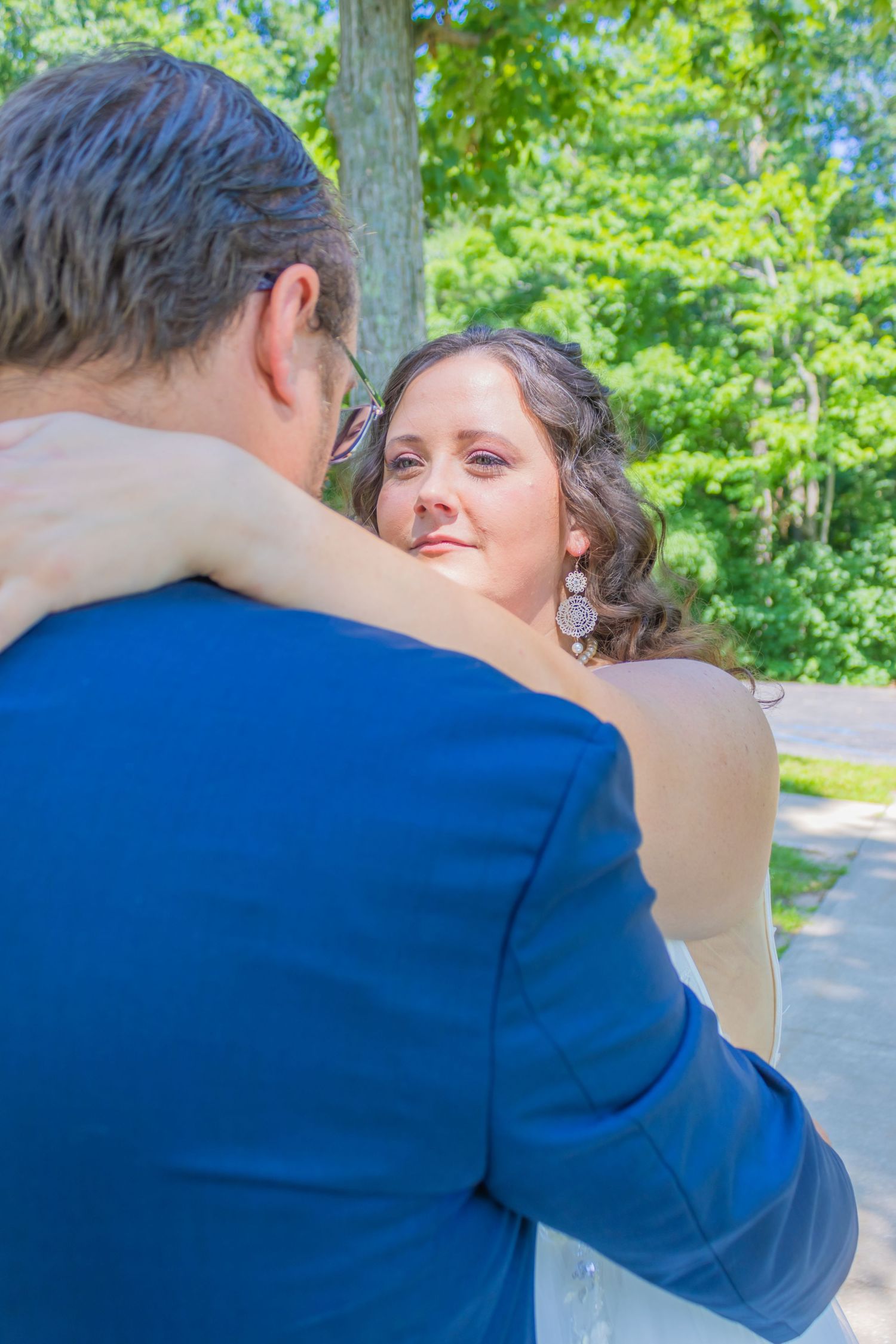 A romantic outdoor wedding moment with the couple embracing in front of green foliage.