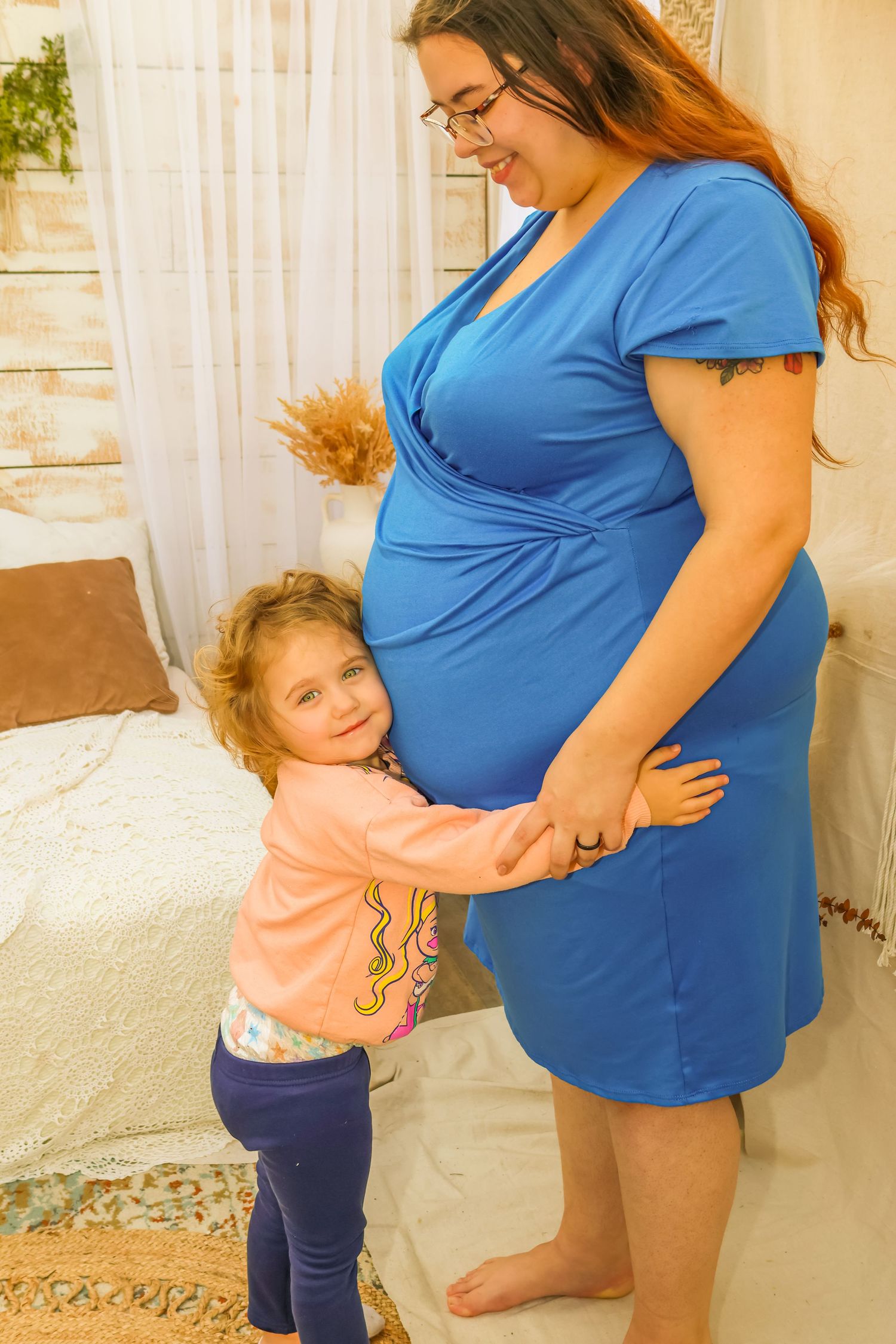 Sweet interaction between young child and pregnant person in blue wrap dress.