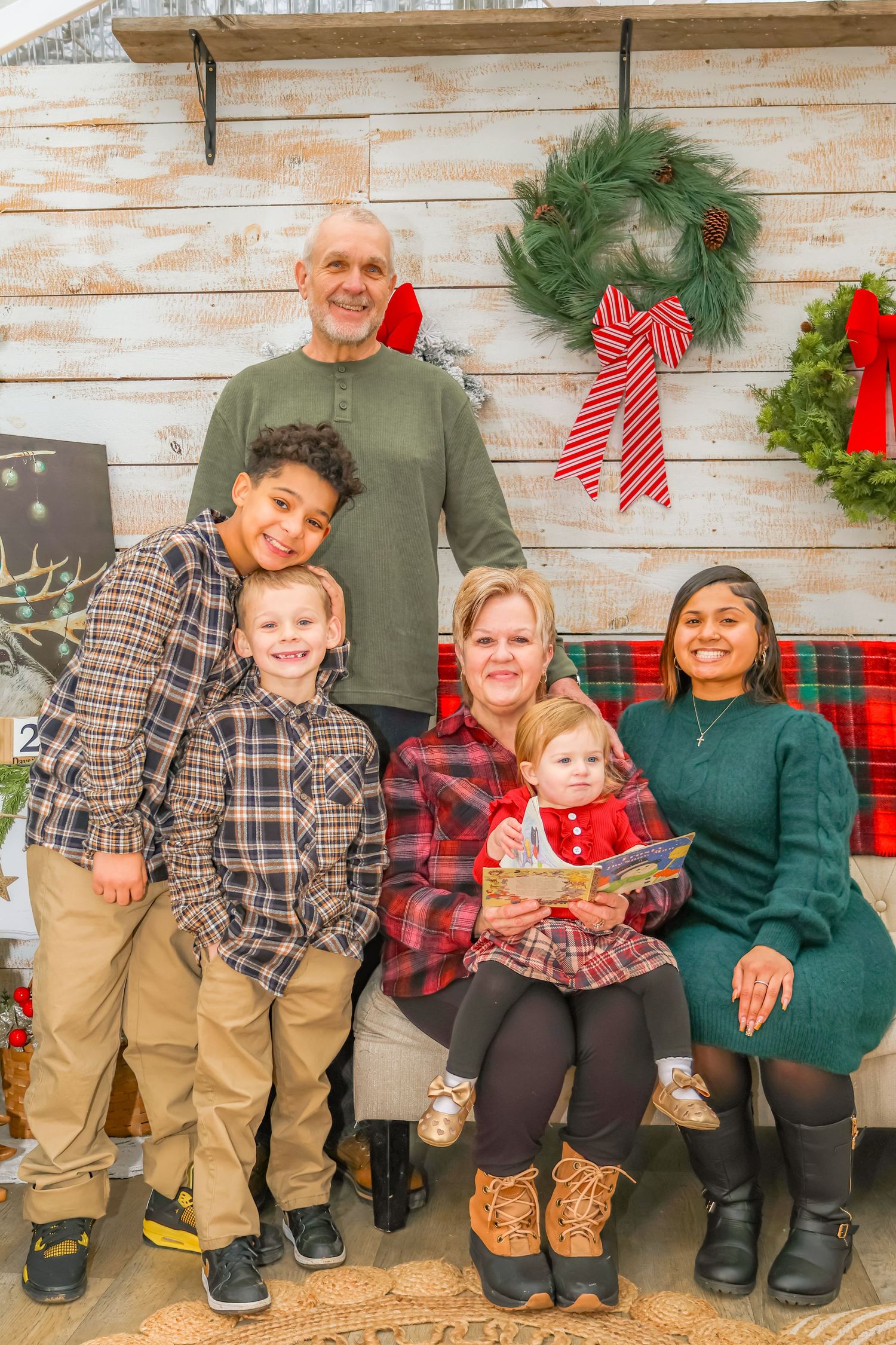 A family holiday portrait with Christmas wreaths and red bows on a rustic white backdrop.