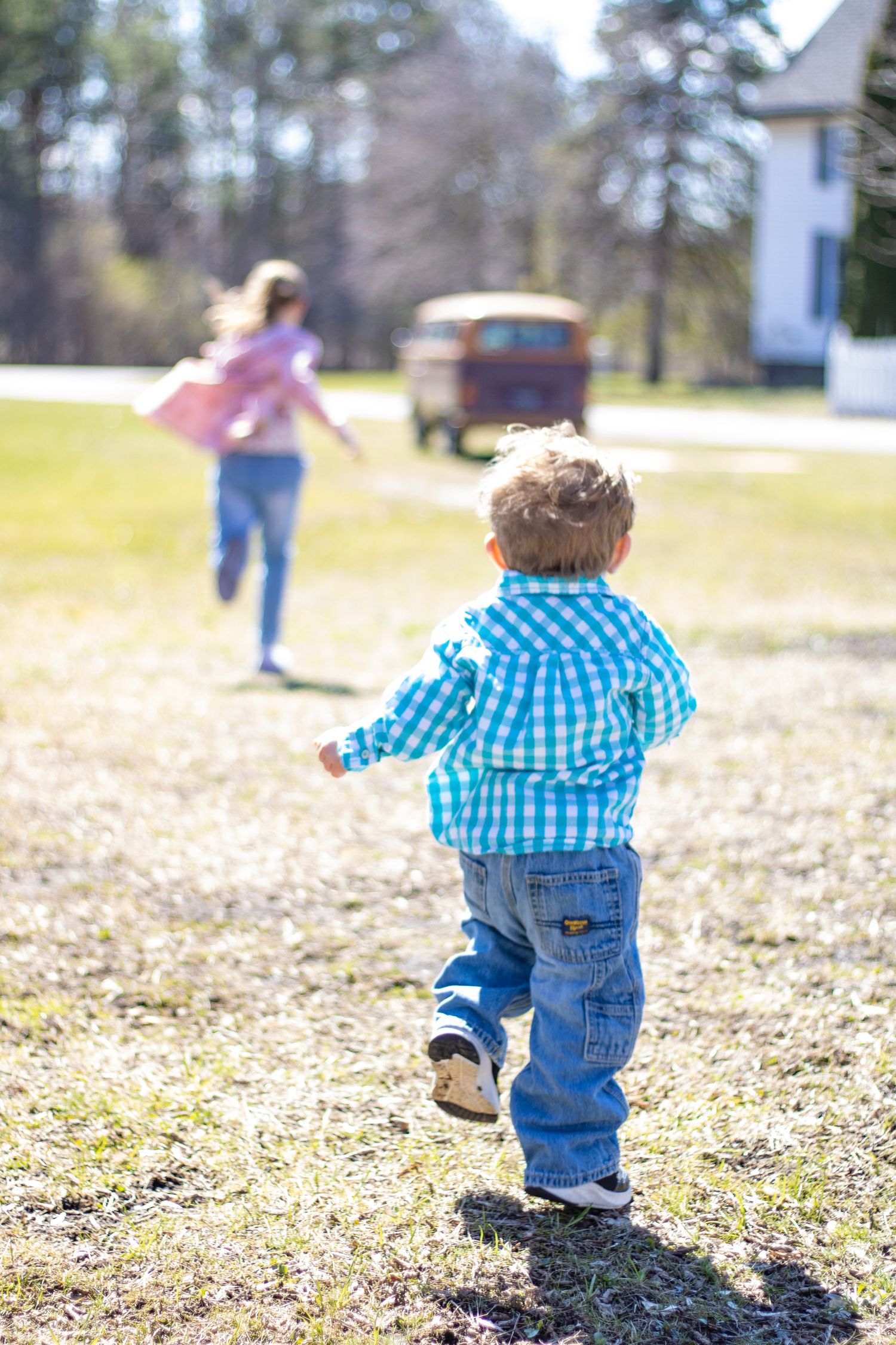 Children running in a field on a sunny day with a red truck in the background.