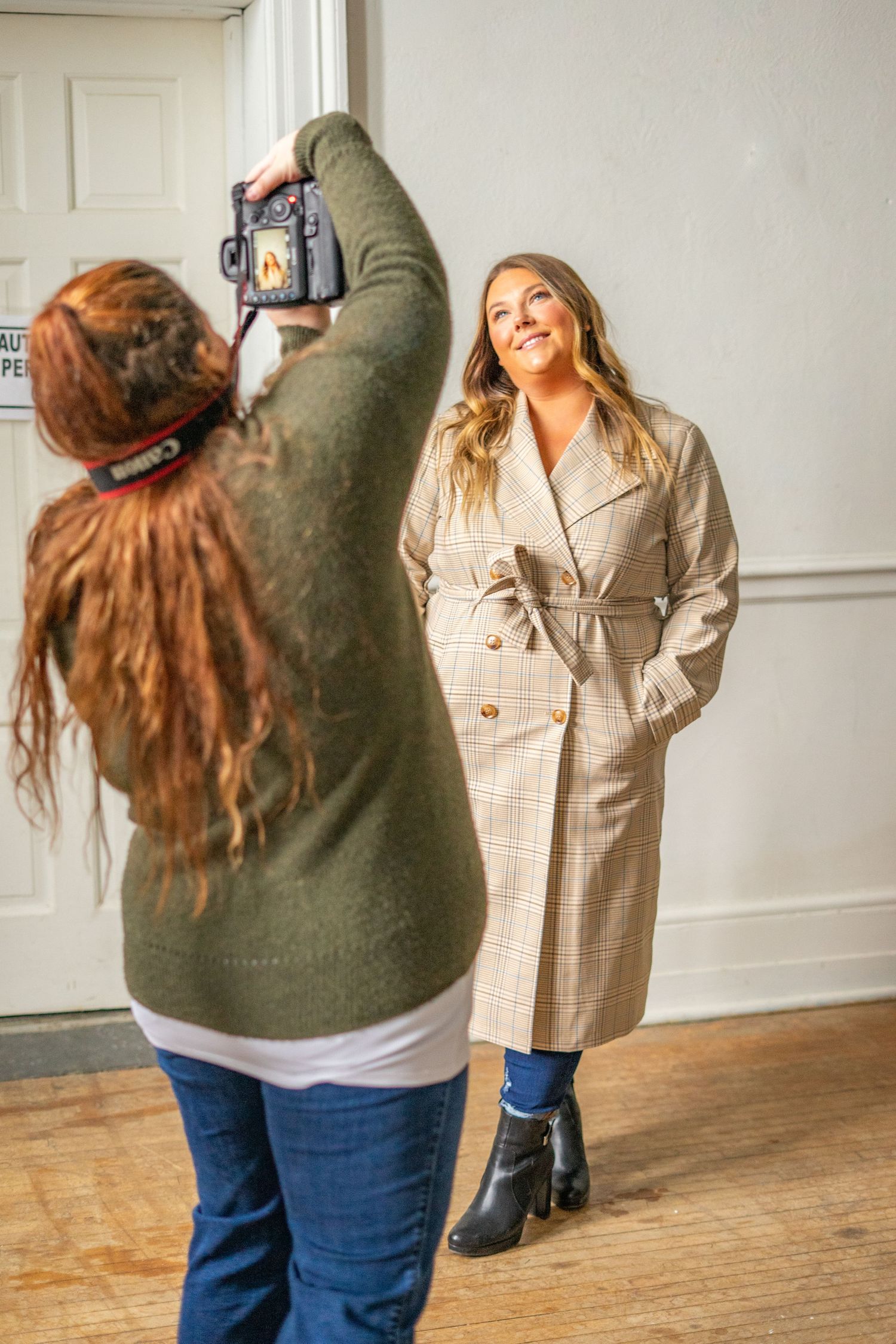 Behind-the-scenes photo of a photography session with someone in a beige trench coat being photographed.