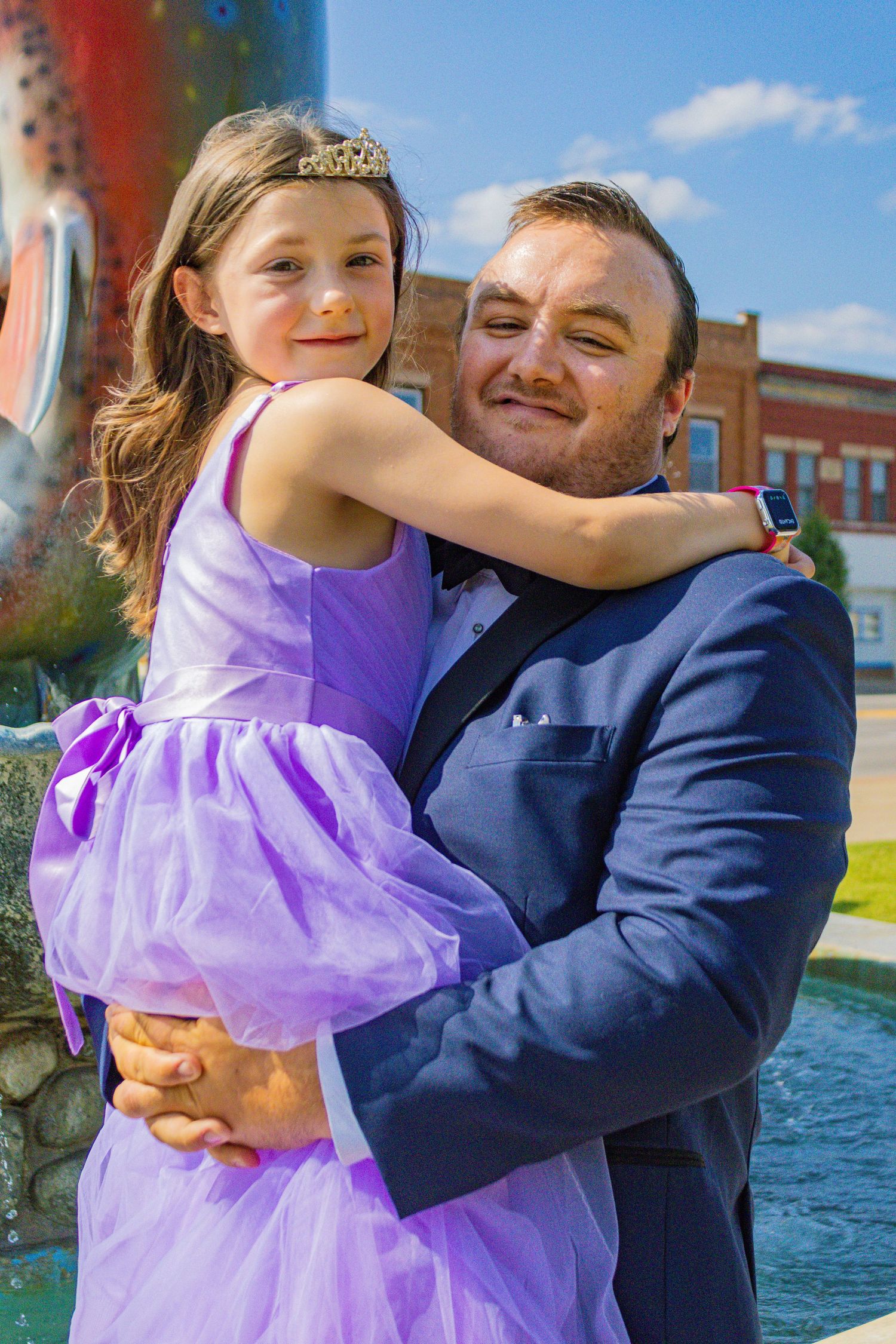 A tender moment between a person in a navy suit and a young girl in a purple tulle dress.
