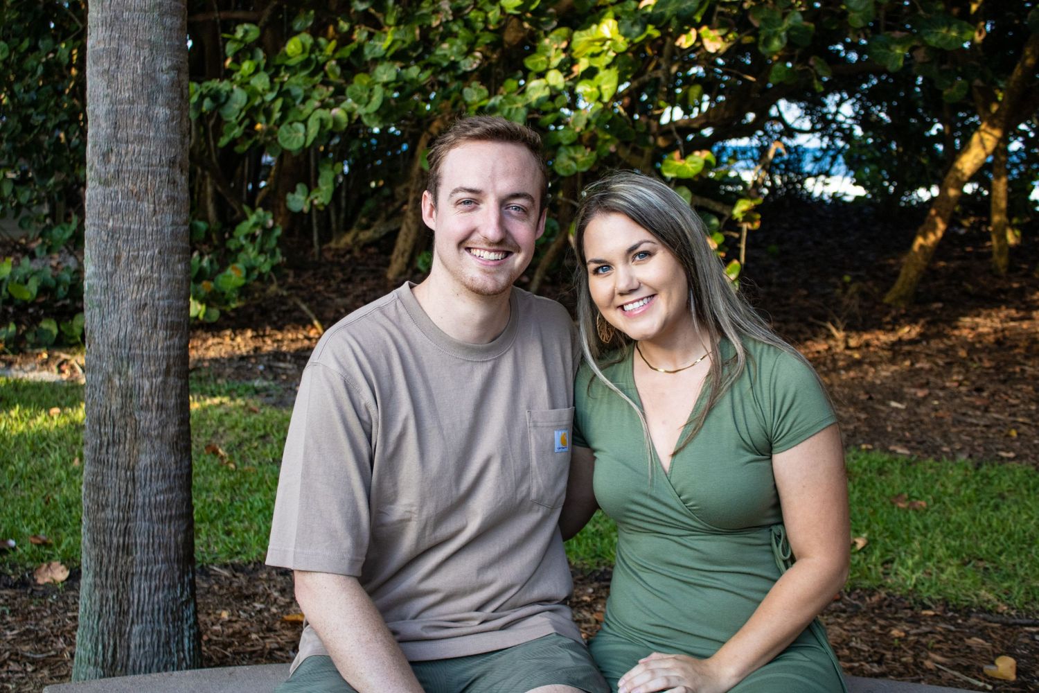 Casual couple sitting outdoors against autumn foliage background.