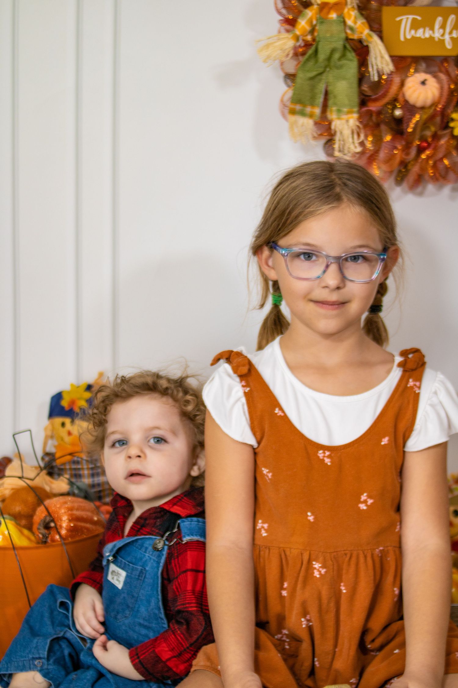 A charming fall scene with children posing among pumpkins and autumn decorations.