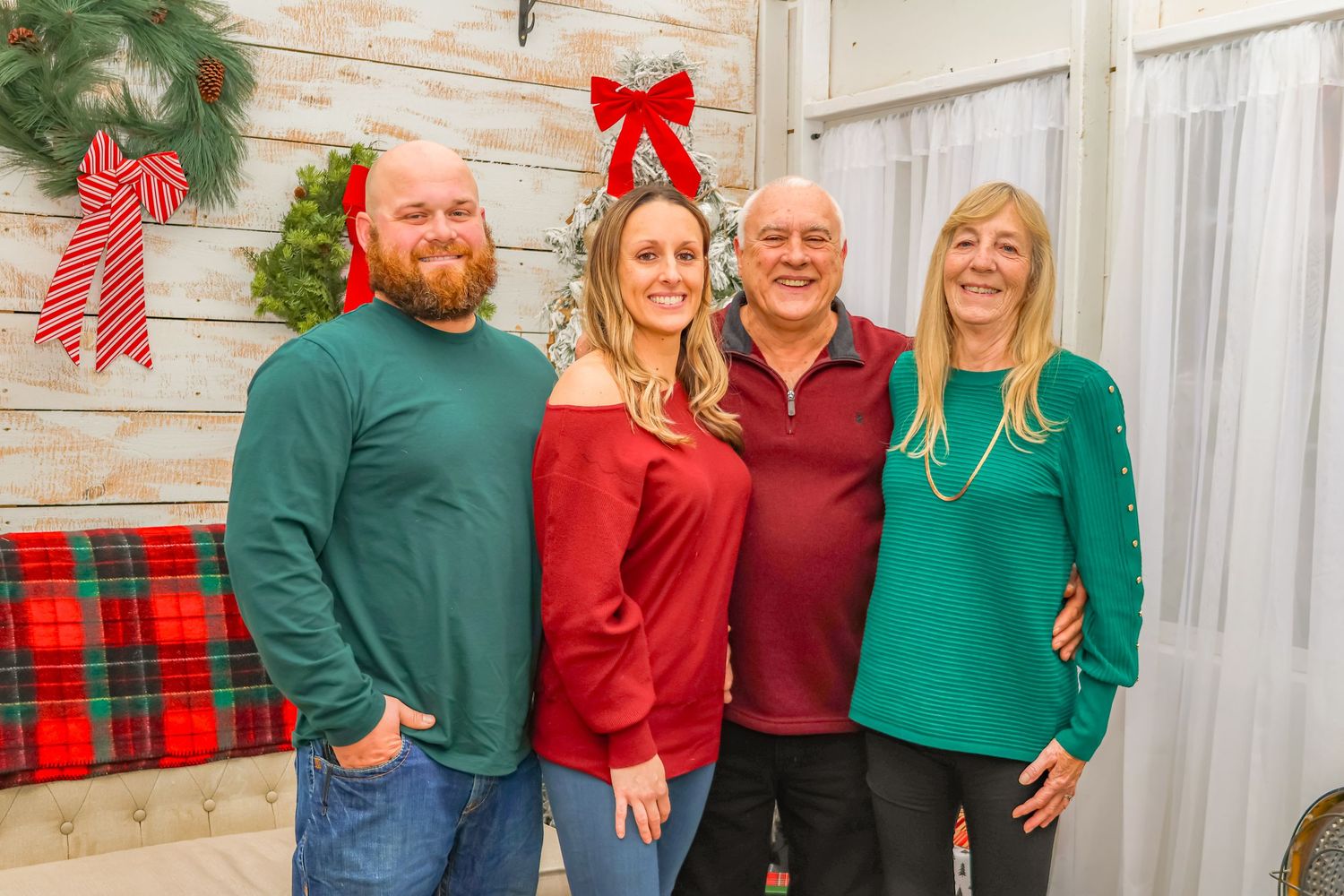 Holiday family photo with coordinated outfits against rustic backdrop with plaid decor.