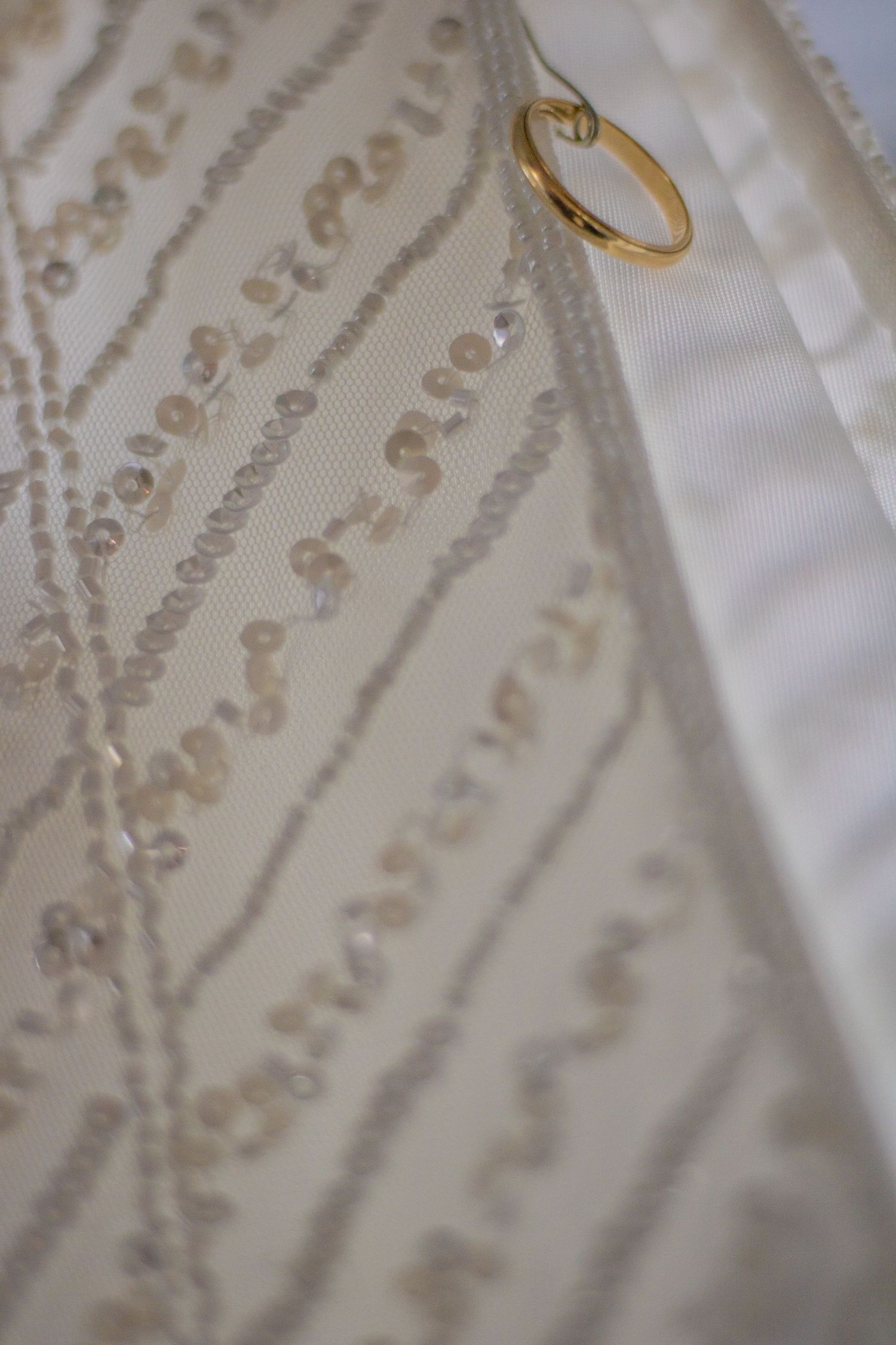 Macro shot of delicate beadwork on a white wedding dress with a gold ring.