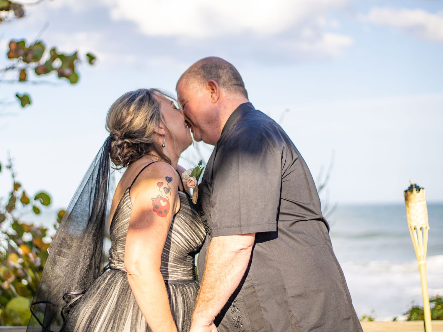Romantic beach wedding moment with green foliage and ocean in background.