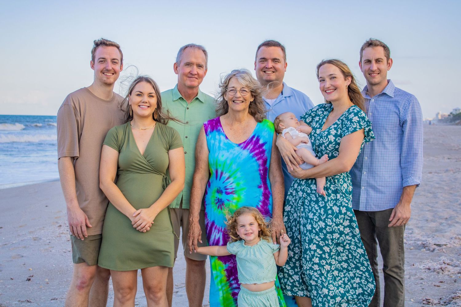 Extended family group poses together on beach at sunset wearing coordinated outfits.