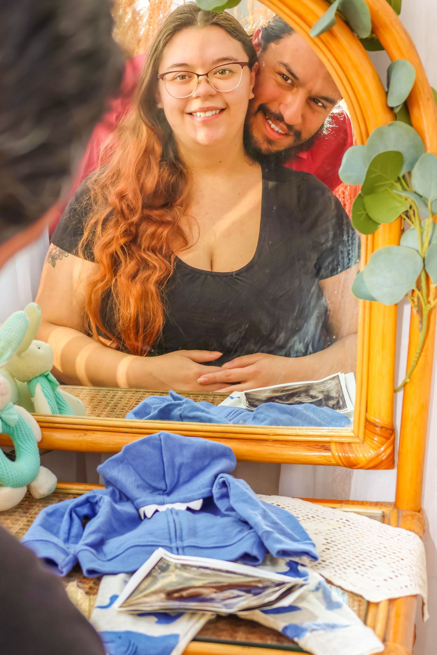 Couple poses together near decorative orange arch with blue fabric and photos visible.