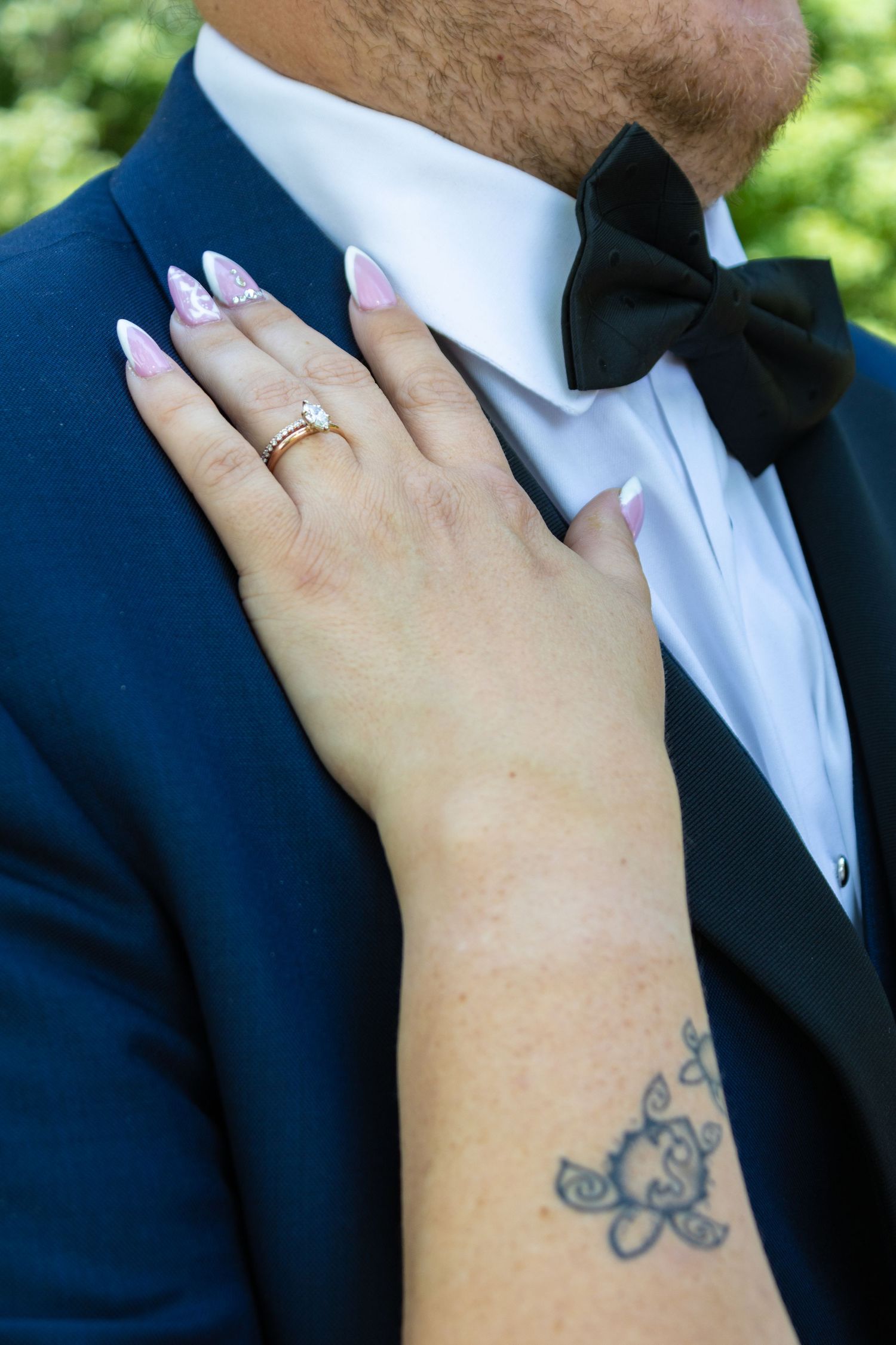 Close up of hand with small tattoo and wedding ring against navy suit with bowtie.