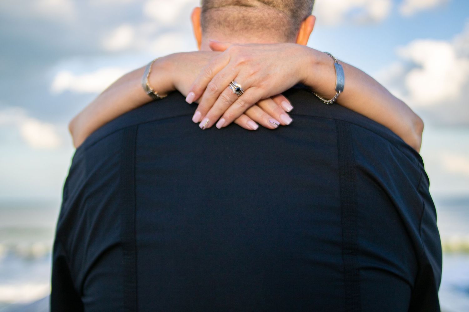 Close-up of hands embracing around shoulders against a blue sky background.