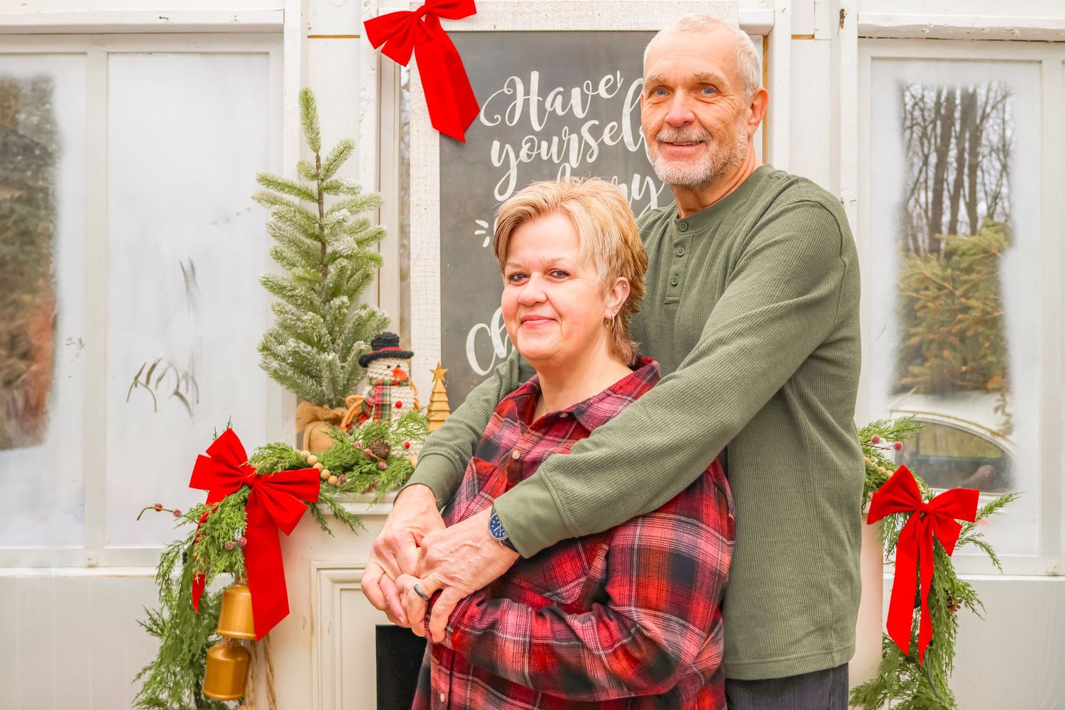 A couple shares a tender moment in front of holiday decorations and greenery.