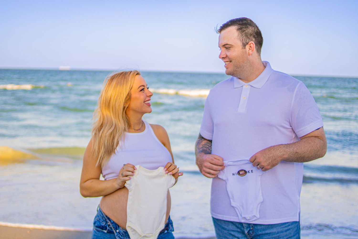 Joyful couple laughing together during beachside maternity photo session.