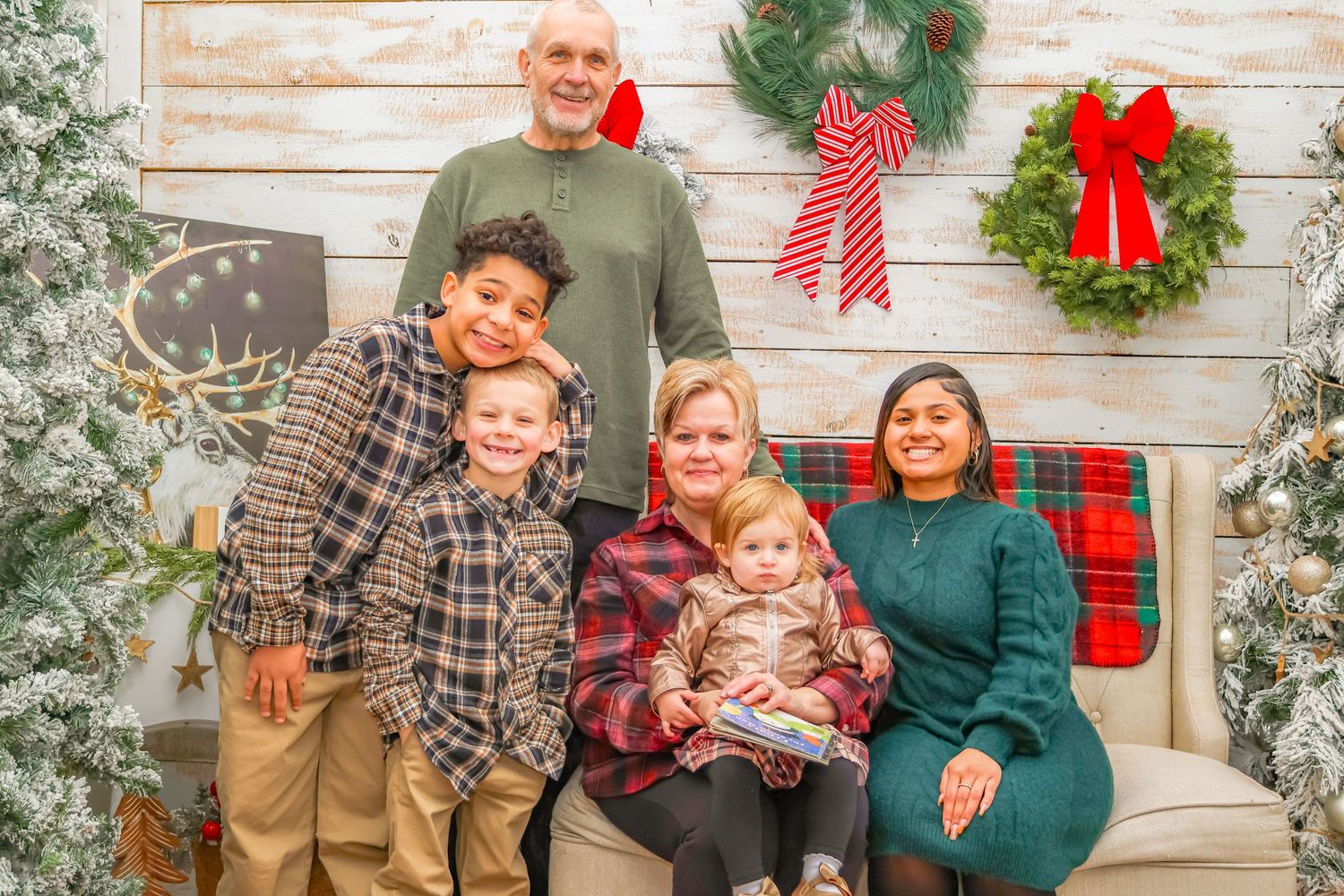A festive family portrait with wreaths and red bows decorating a rustic white wall behind them.