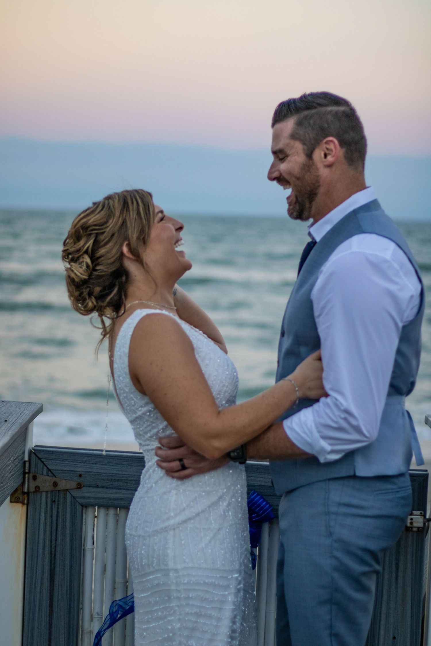 A wedding couple shares an intimate moment at sunset on a beach boardwalk.