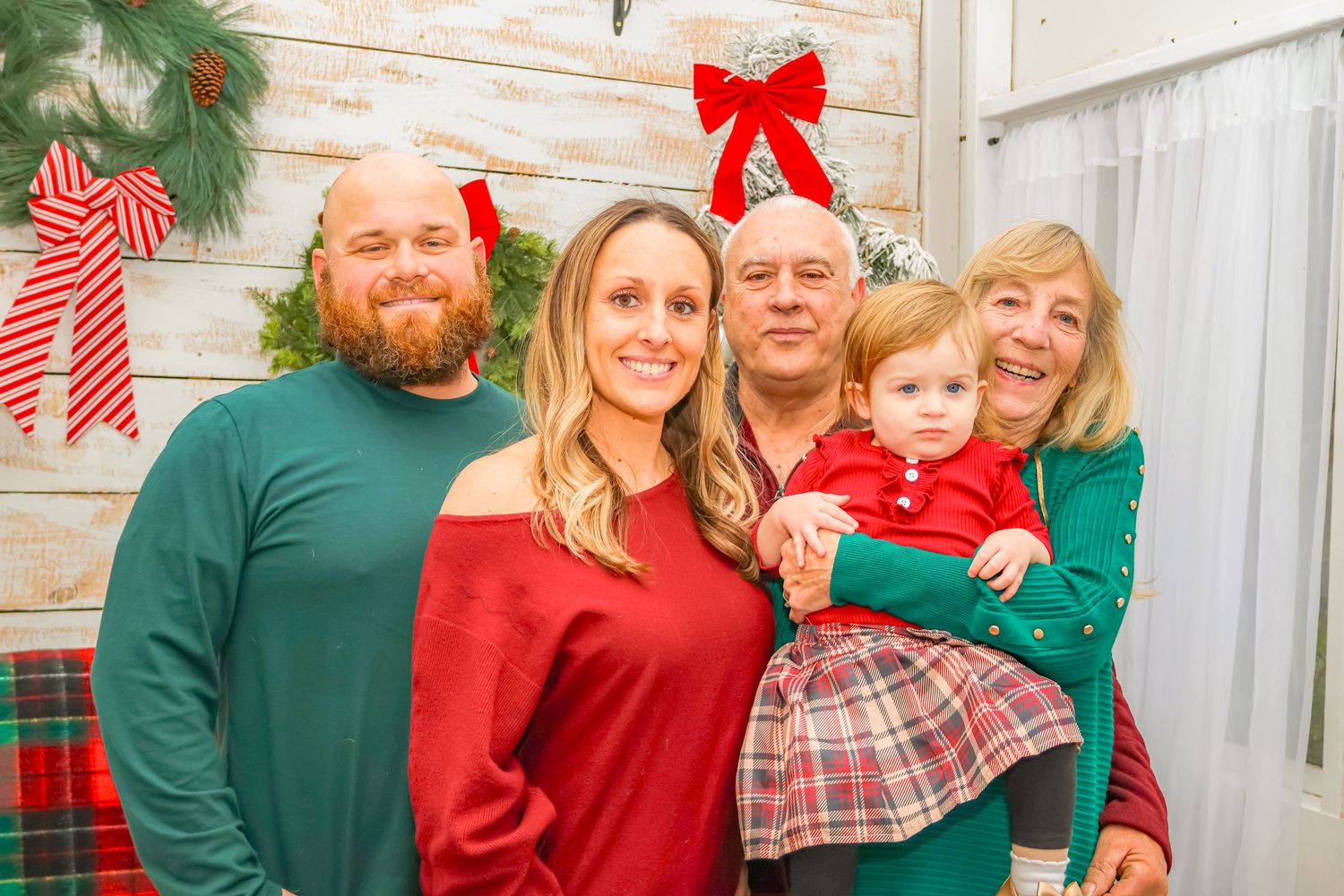 Family holiday portrait in coordinated red and green outfits against a rustic white backdrop.