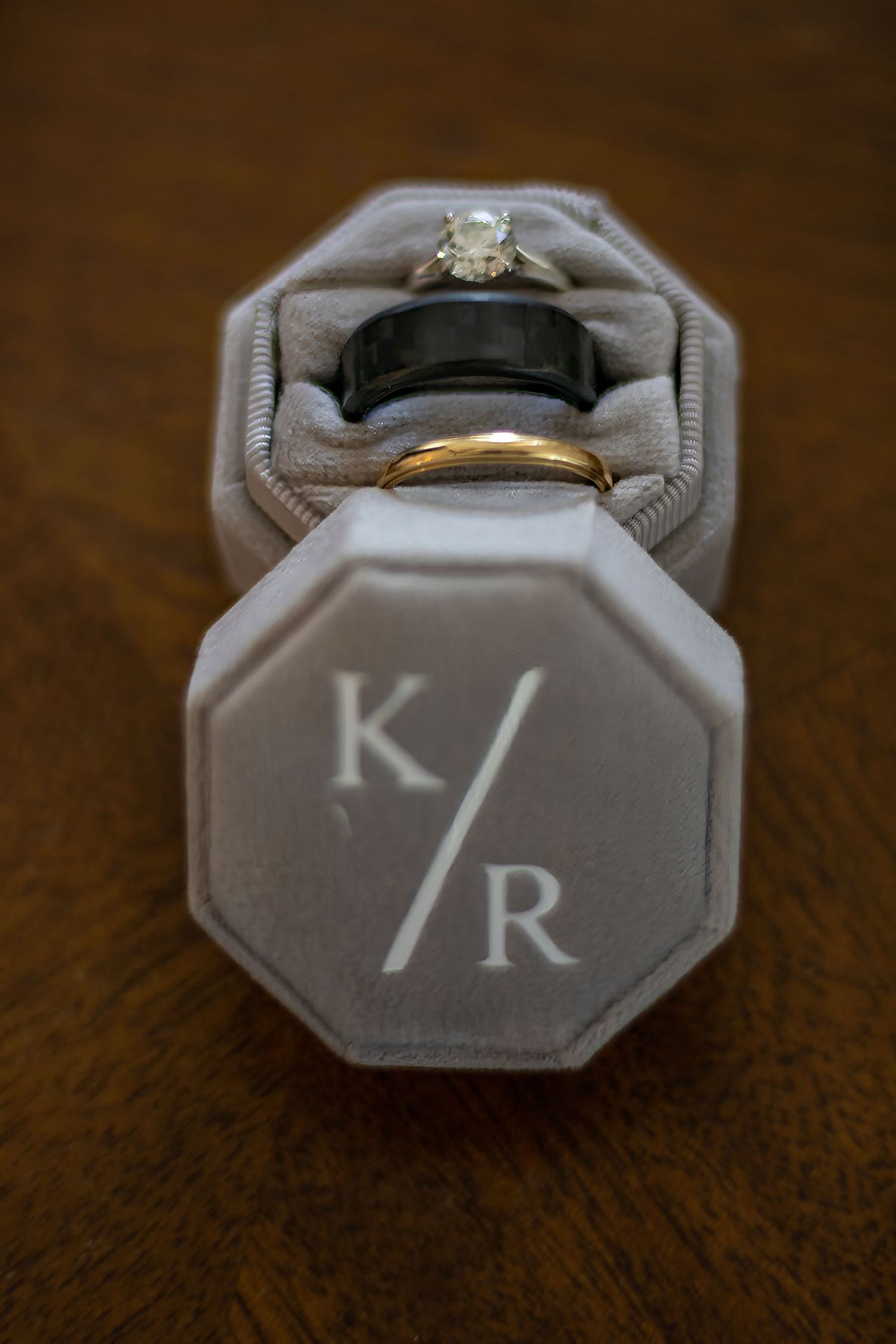 Wedding rings displayed in a gray monogrammed ring box with K/R initials.