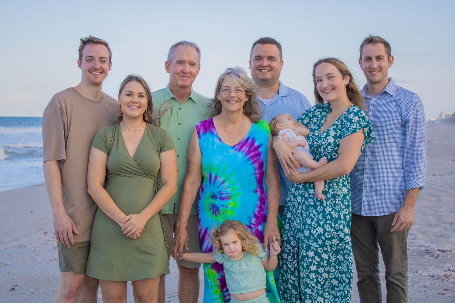 A multi-generational family gathered for a portrait on the beach at sunset.